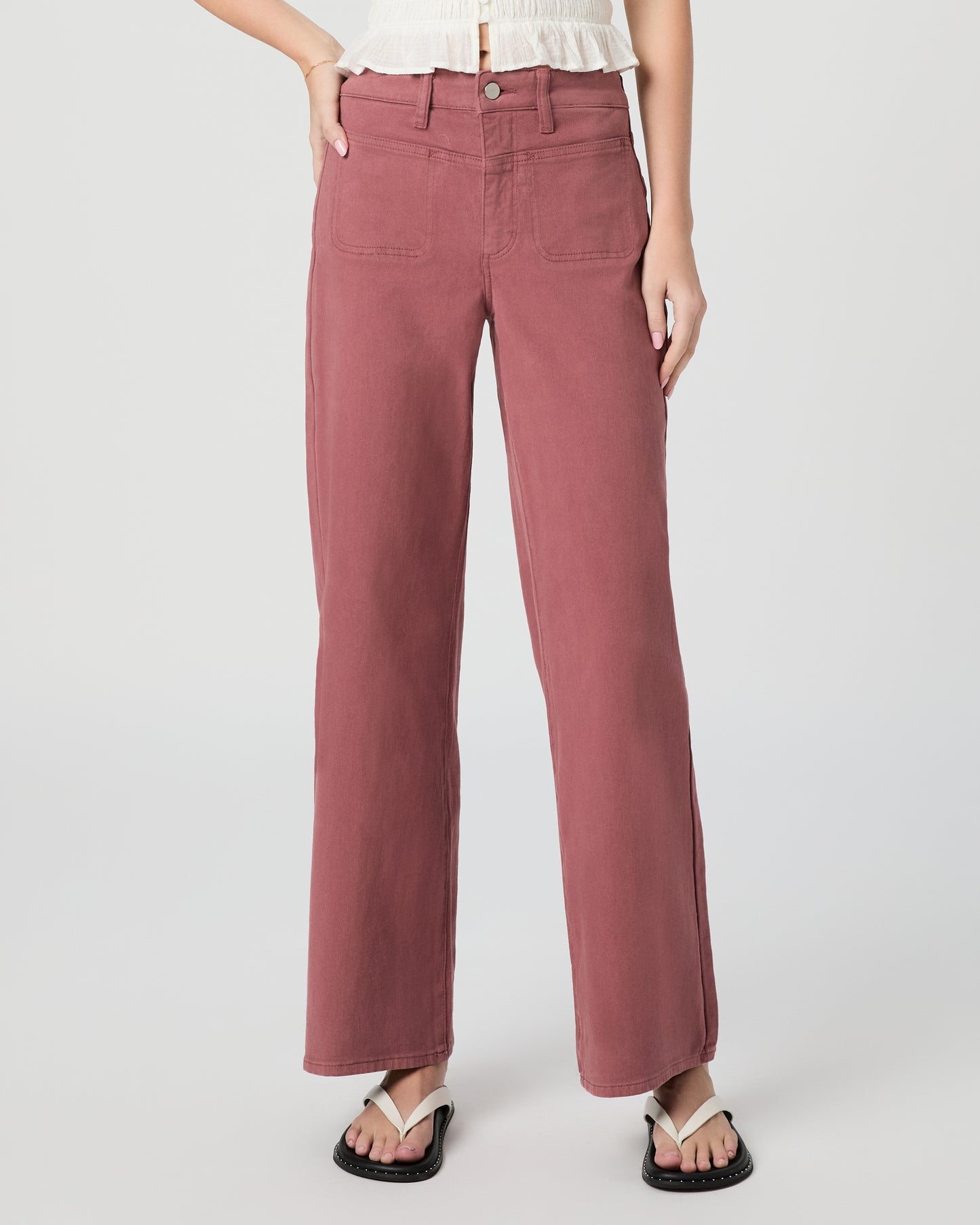 Woman wearing a white blouse and pink jeans paired with white sandals on a gray background