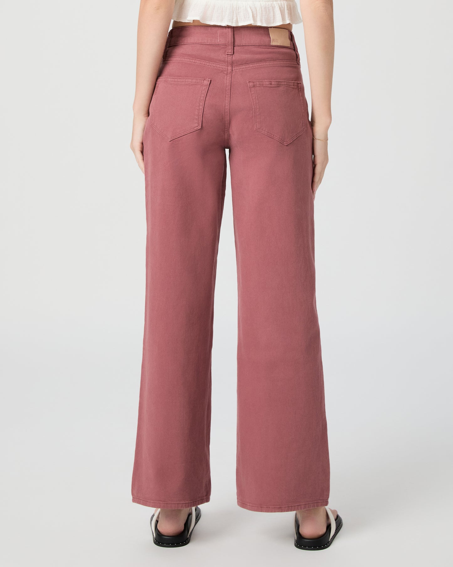 Woman wearing a white blouse and pink jeans paired with white sandals on a gray background