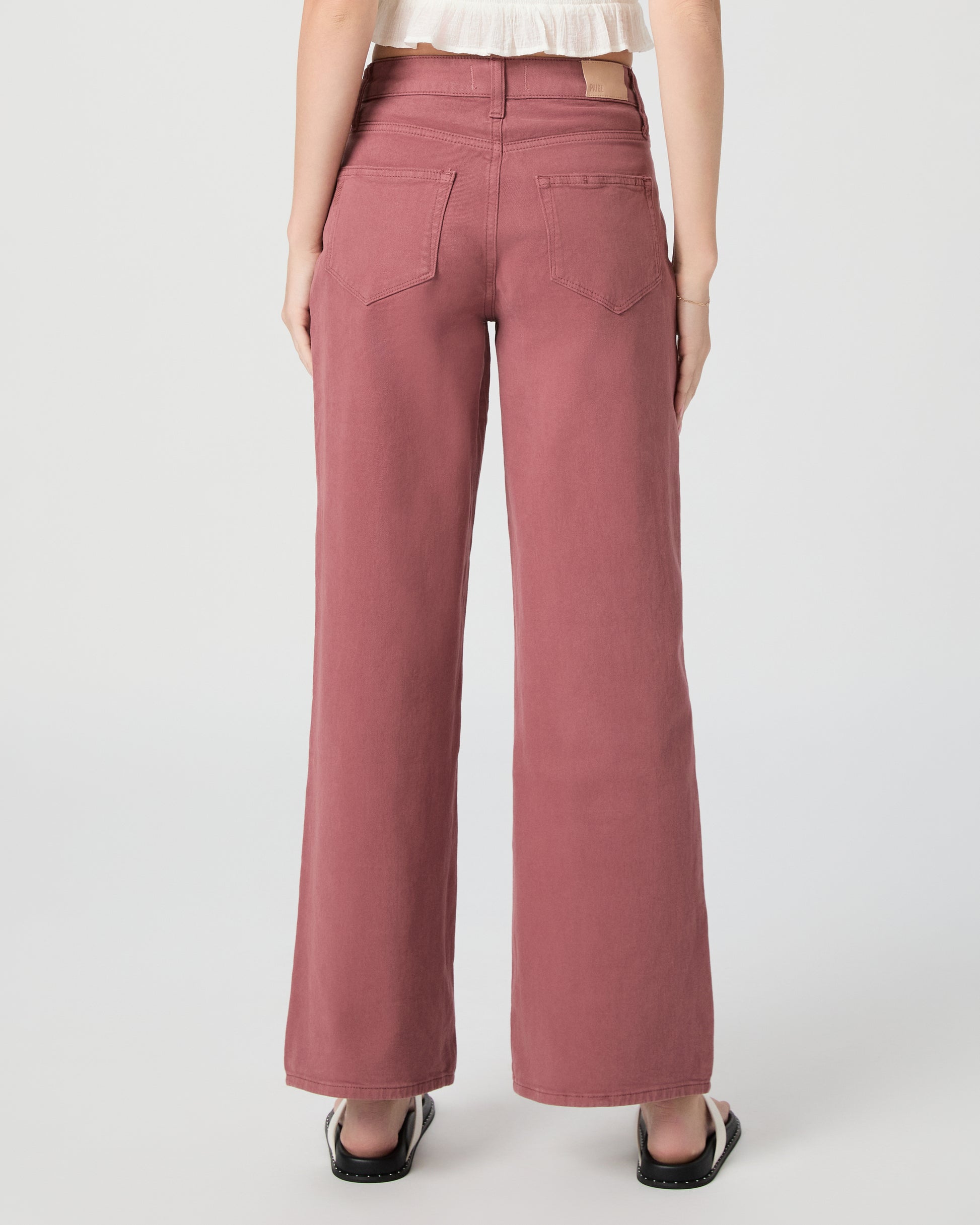 Woman wearing a white blouse and pink jeans paired with white sandals on a gray background