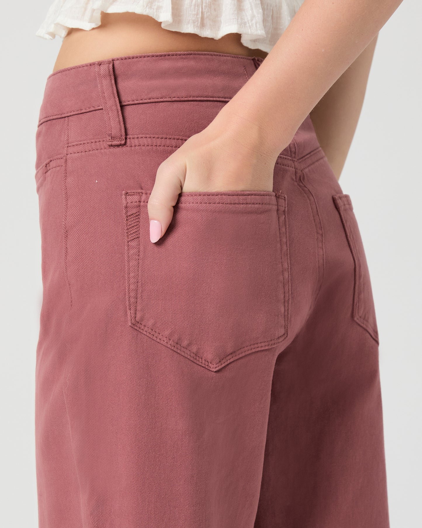 Woman wearing a white blouse and pink jeans paired with white sandals on a gray background