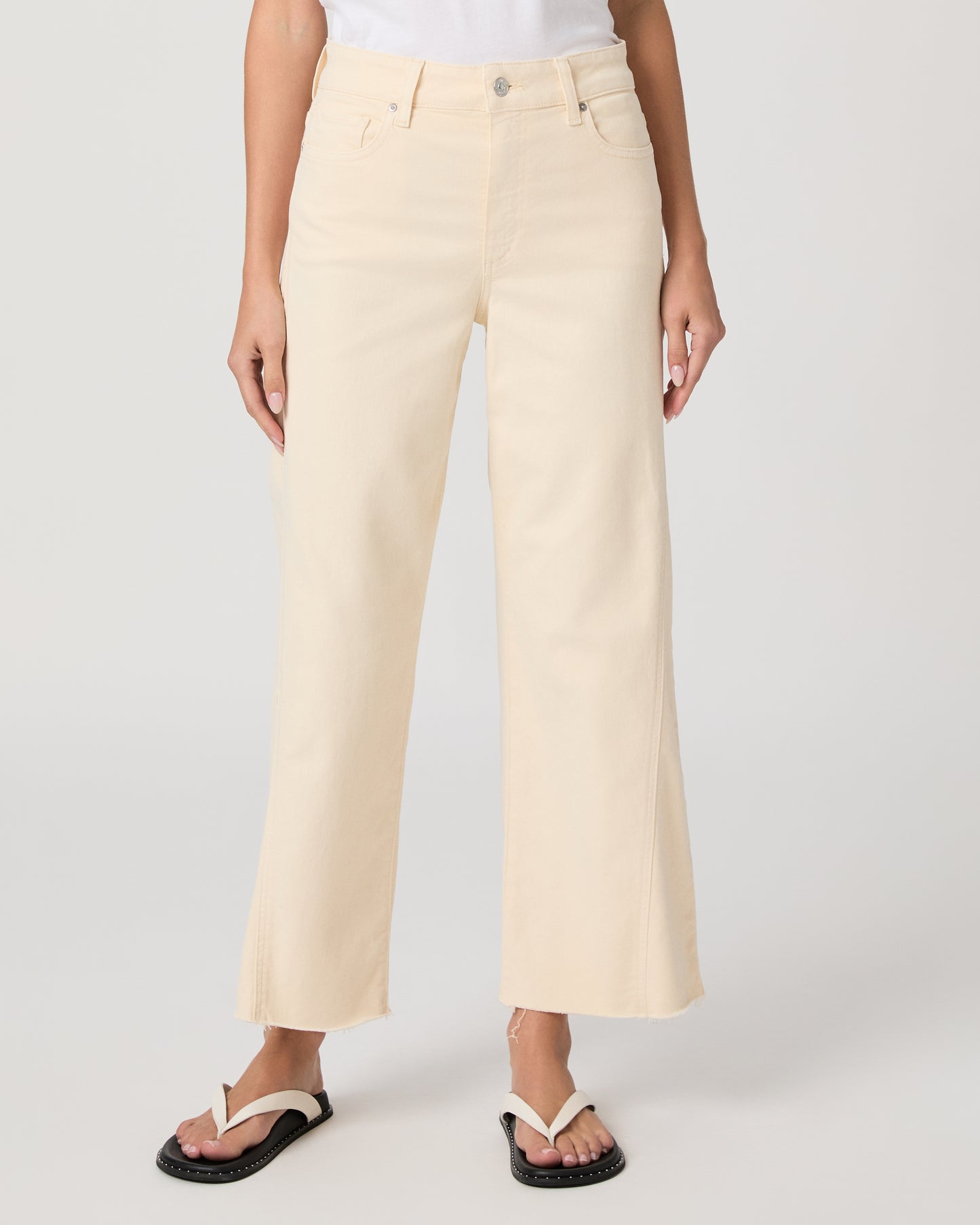 Woman wearing a white top and light yellow jeans on a white background