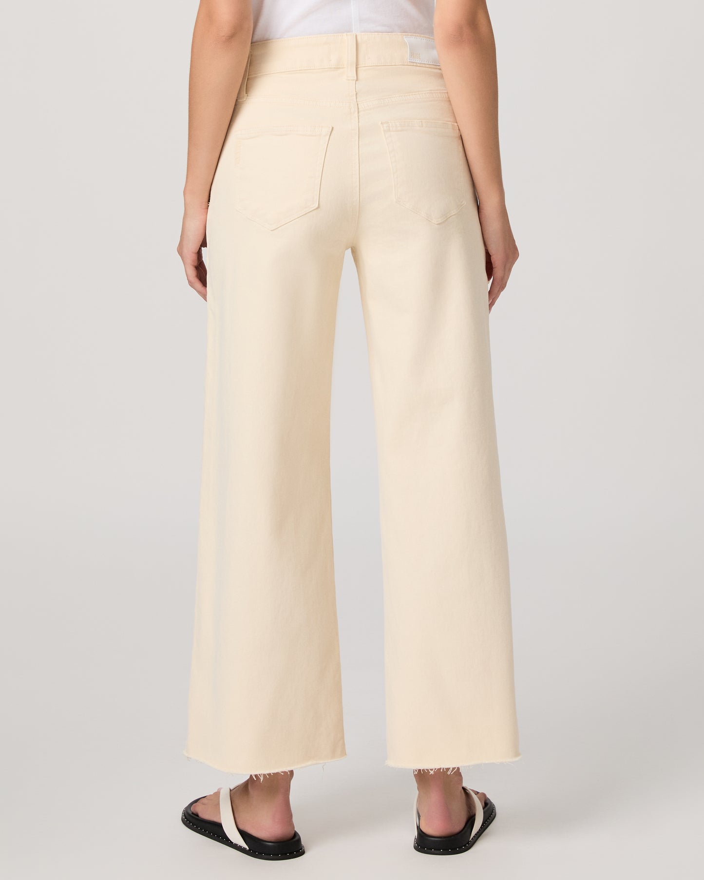 Woman wearing a white top and light yellow jeans on a white background