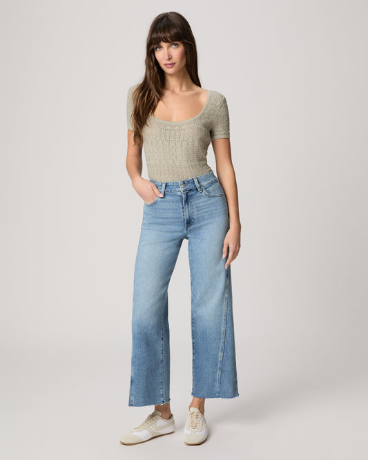 Woman wearing a light green top and blue jeans on a white background