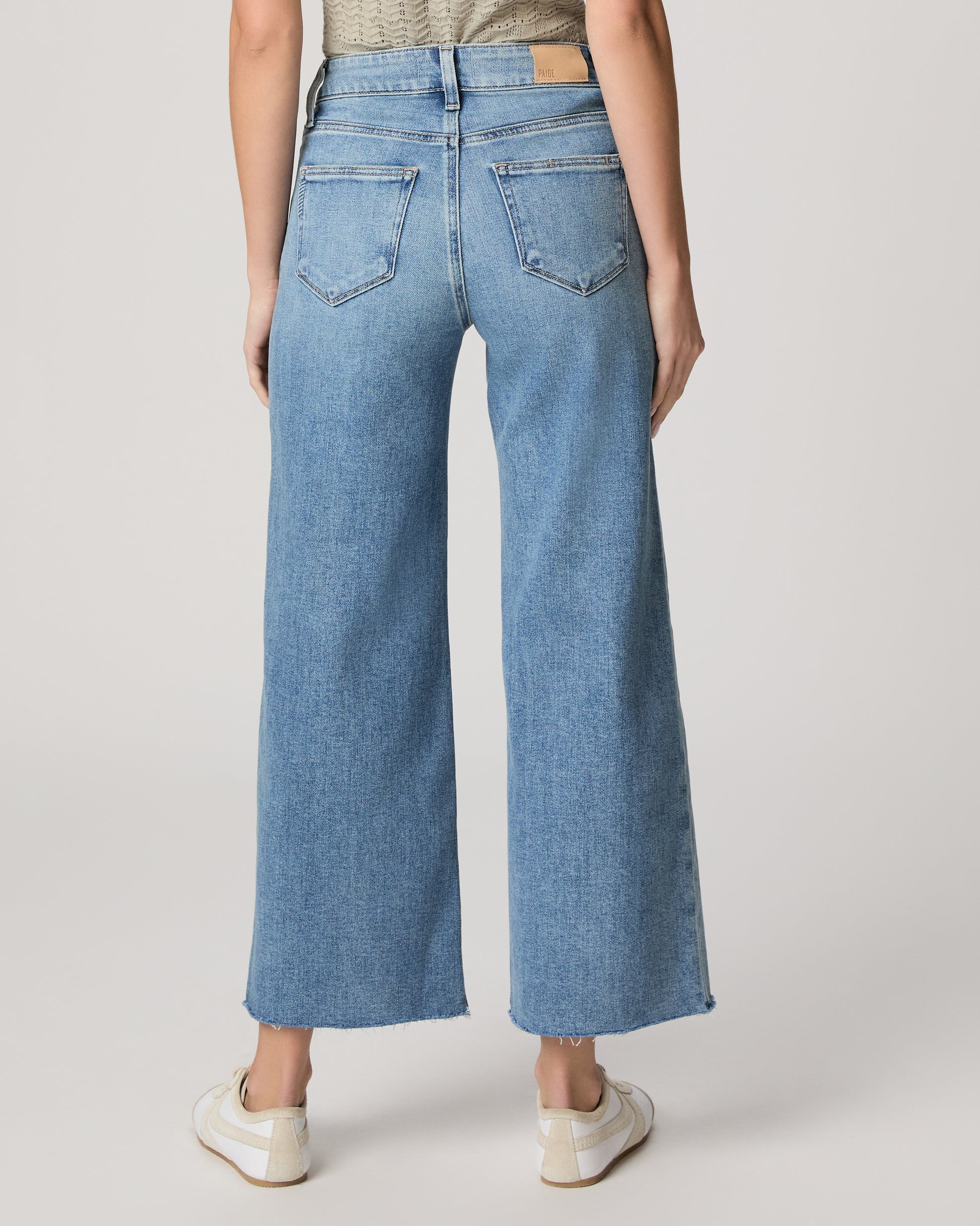 Woman wearing a light green top and blue jeans on a white background