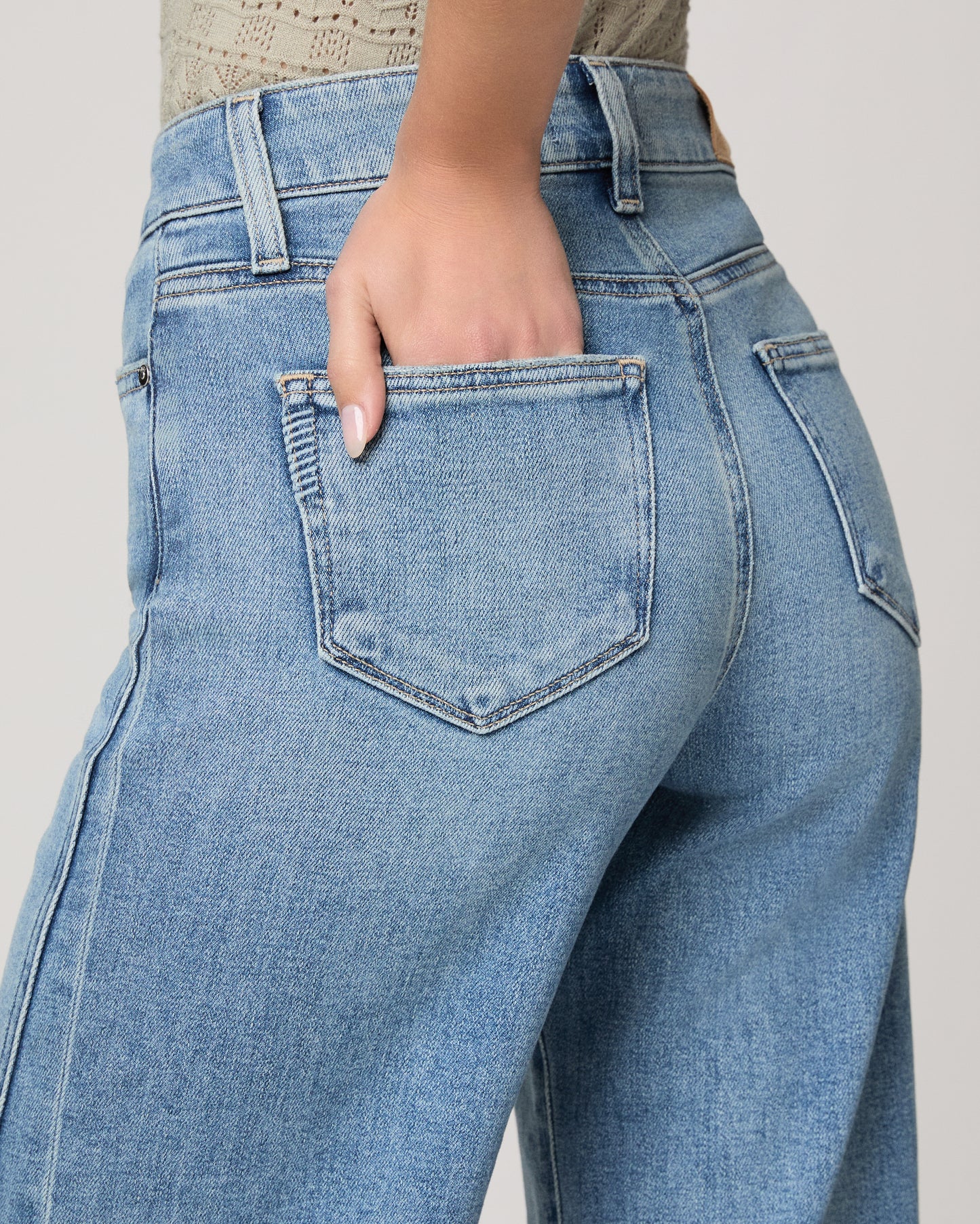 Woman wearing a light green top and blue jeans on a white background