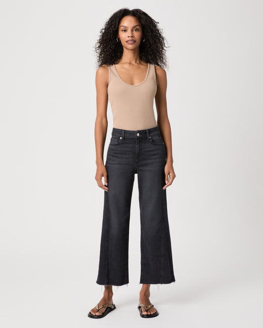 women wearing a beige top paired with black jeans and snake print sandals against a white background 