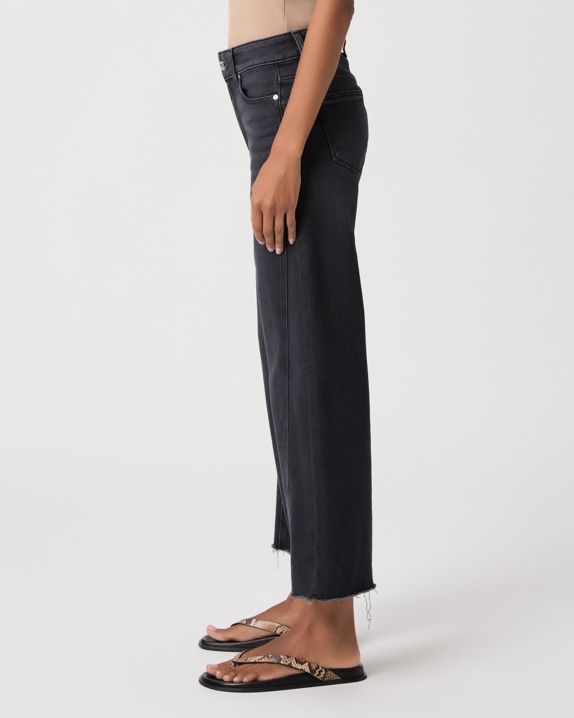 women wearing a beige top paired with black jeans and snake print sandals against a white background 