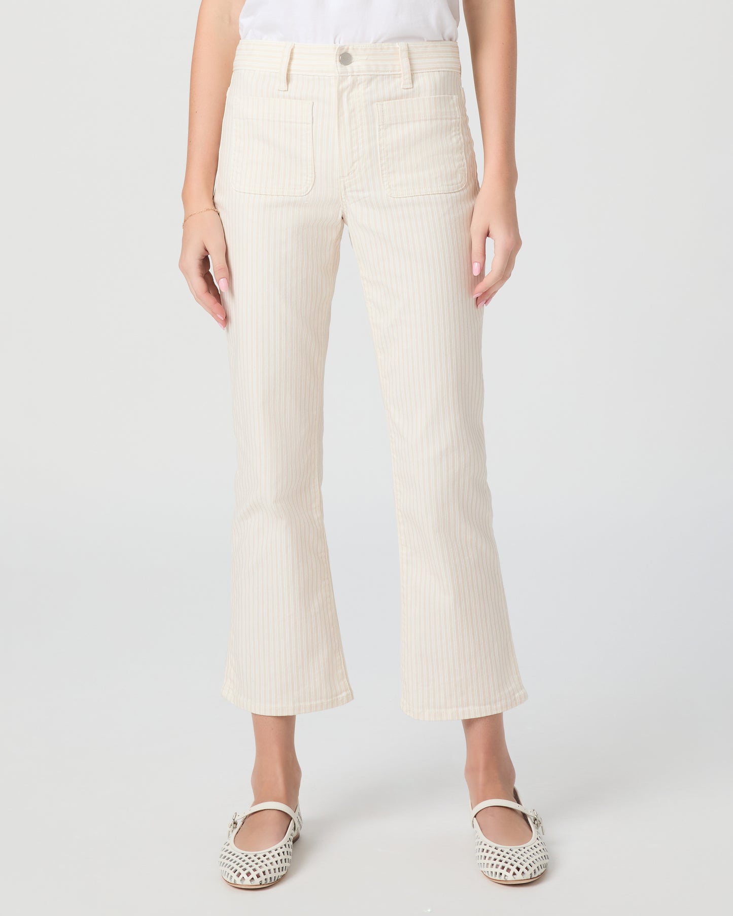 Woman wearing a white t-shirt and cream pants paired with white flats on a plain background