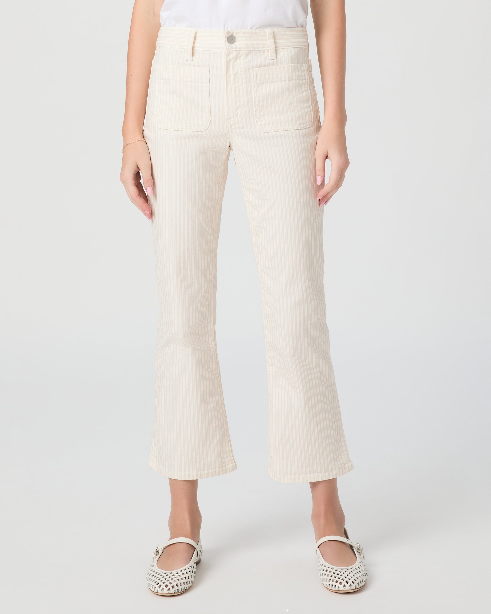 Woman wearing a white t-shirt and cream pants paired with white flats on a plain background