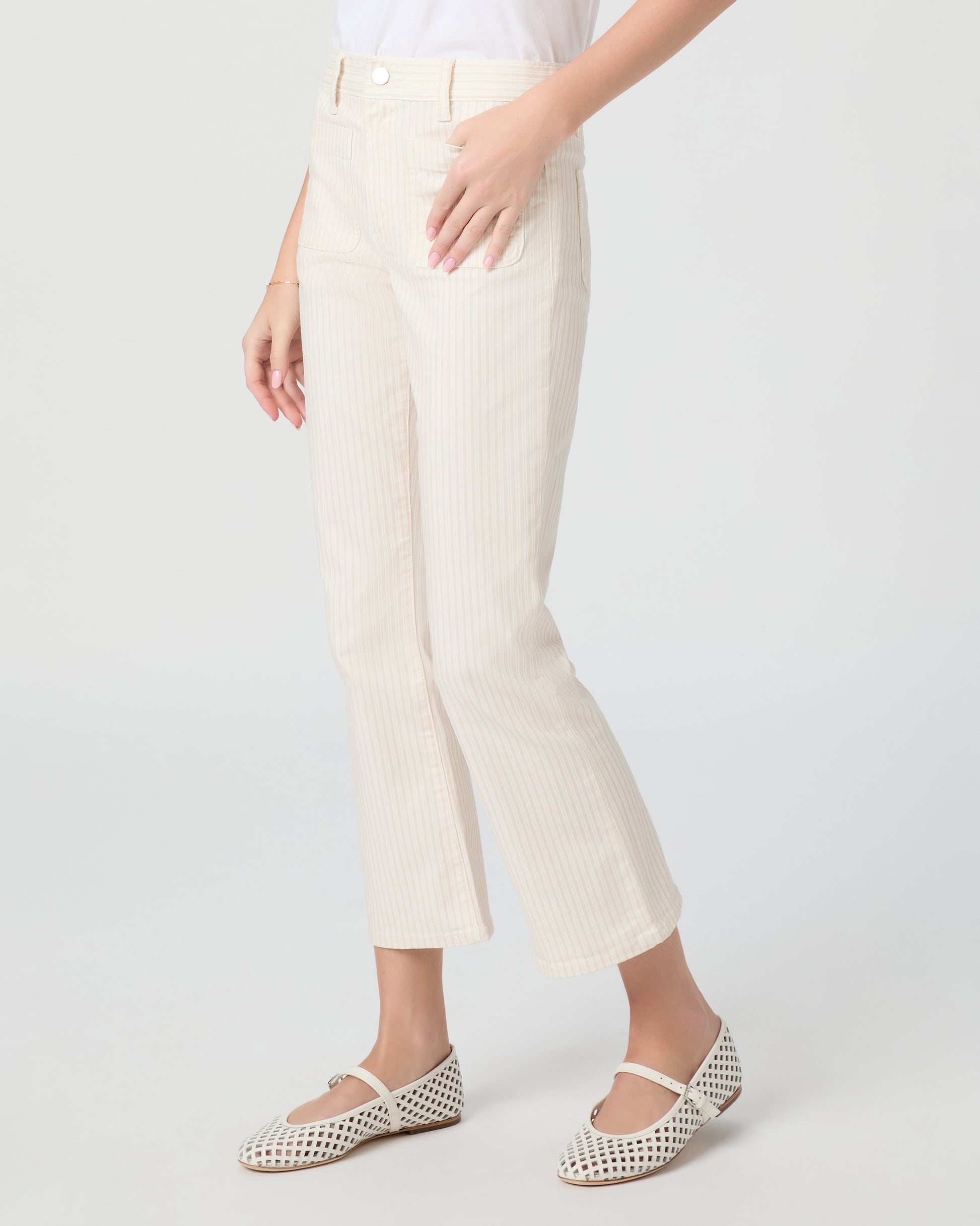 Woman wearing a white t-shirt and cream pants paired with white flats on a plain background