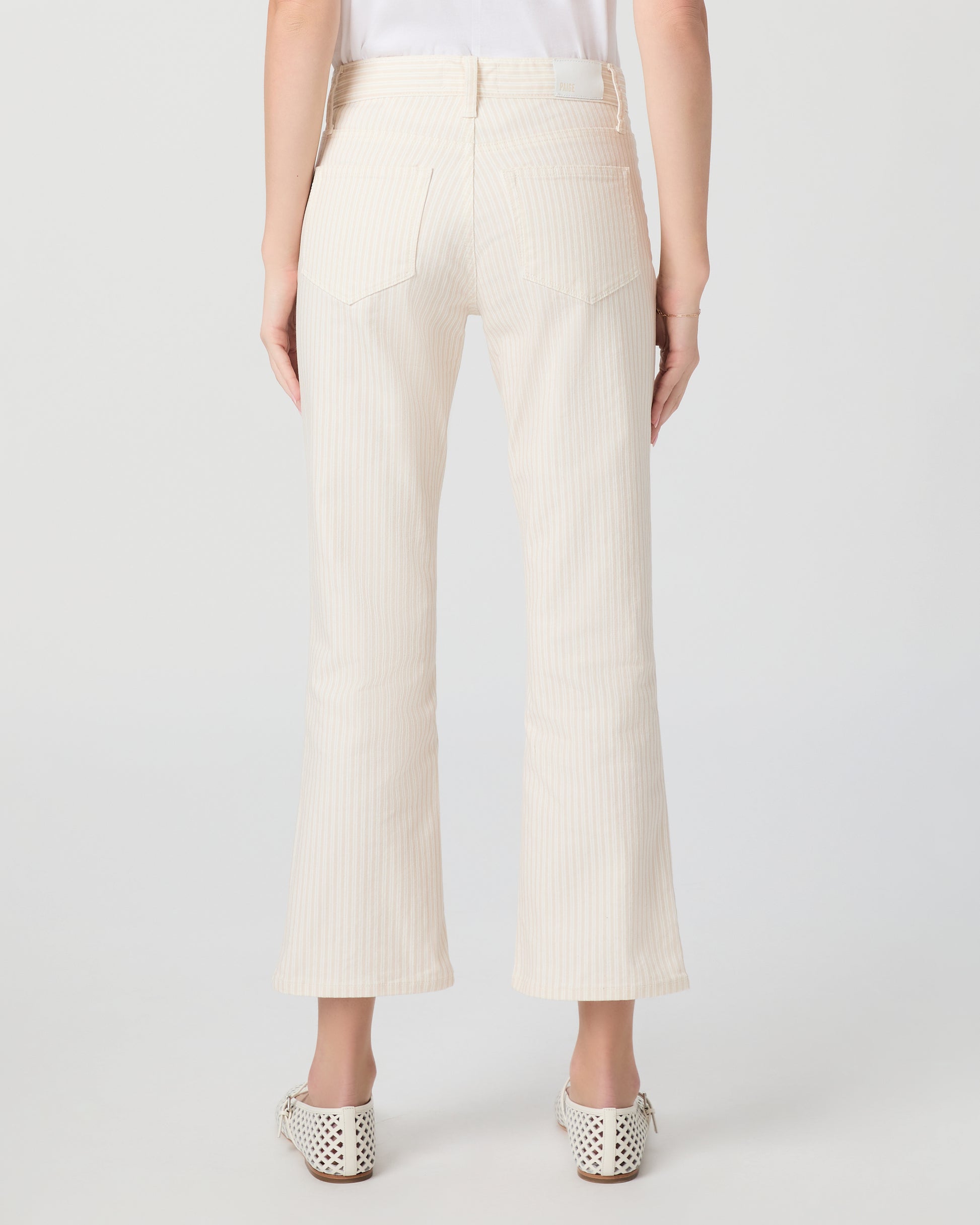 Woman wearing a white t-shirt and cream pants paired with white flats on a plain background