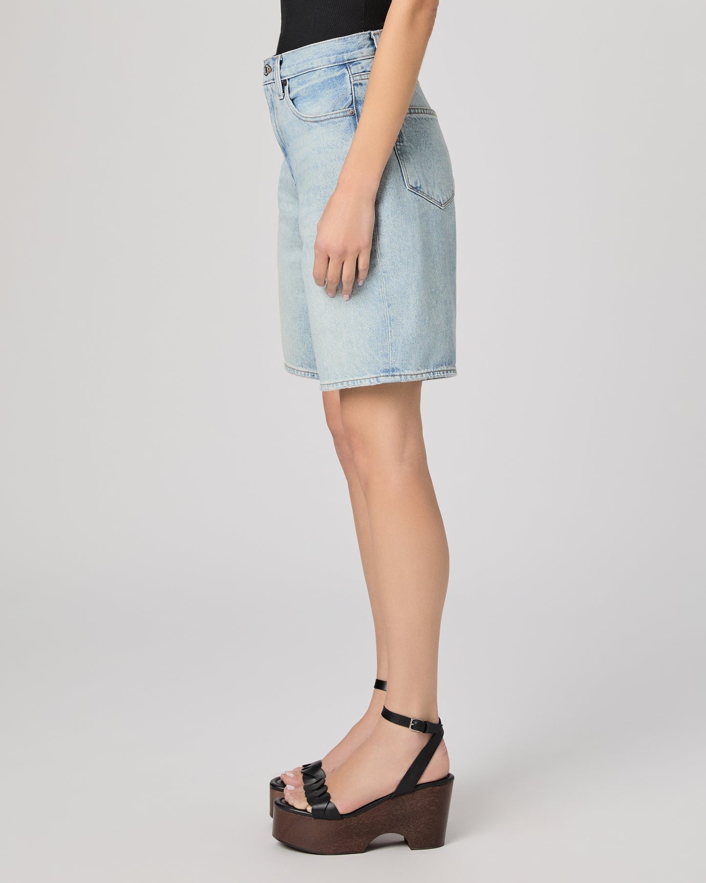 Woman wearing a black sleeveless top and light blue denim shorts paired with black heels on a gray background