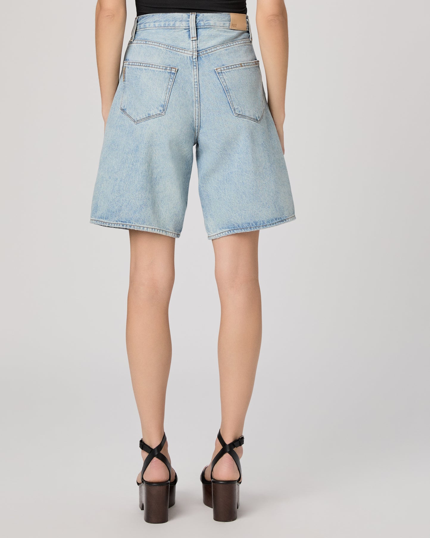 Woman wearing a black sleeveless top and light blue denim shorts paired with black heels on a gray background