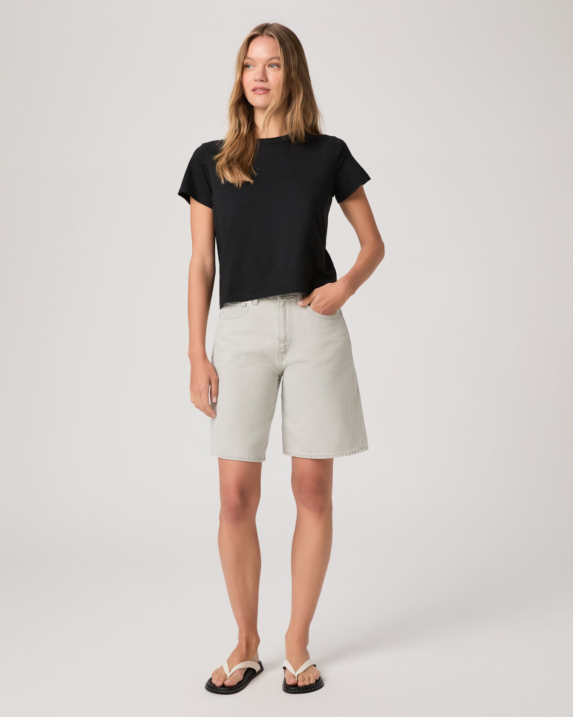 Woman wearing a black top and grey shorts on a white background