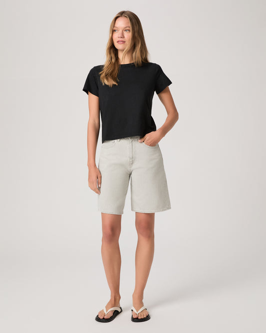 Woman wearing a black top and grey shorts on a white background