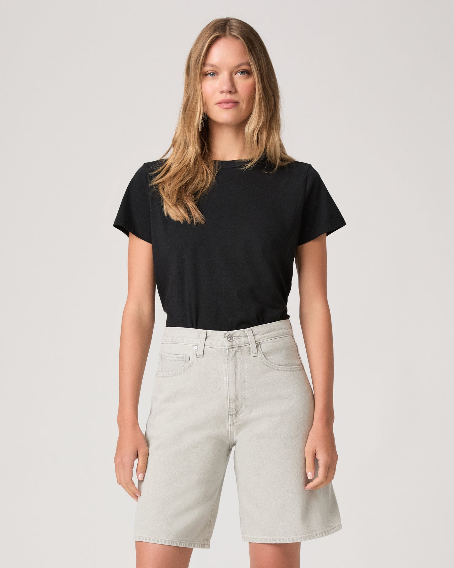 Woman wearing a black top and grey shorts on a white background