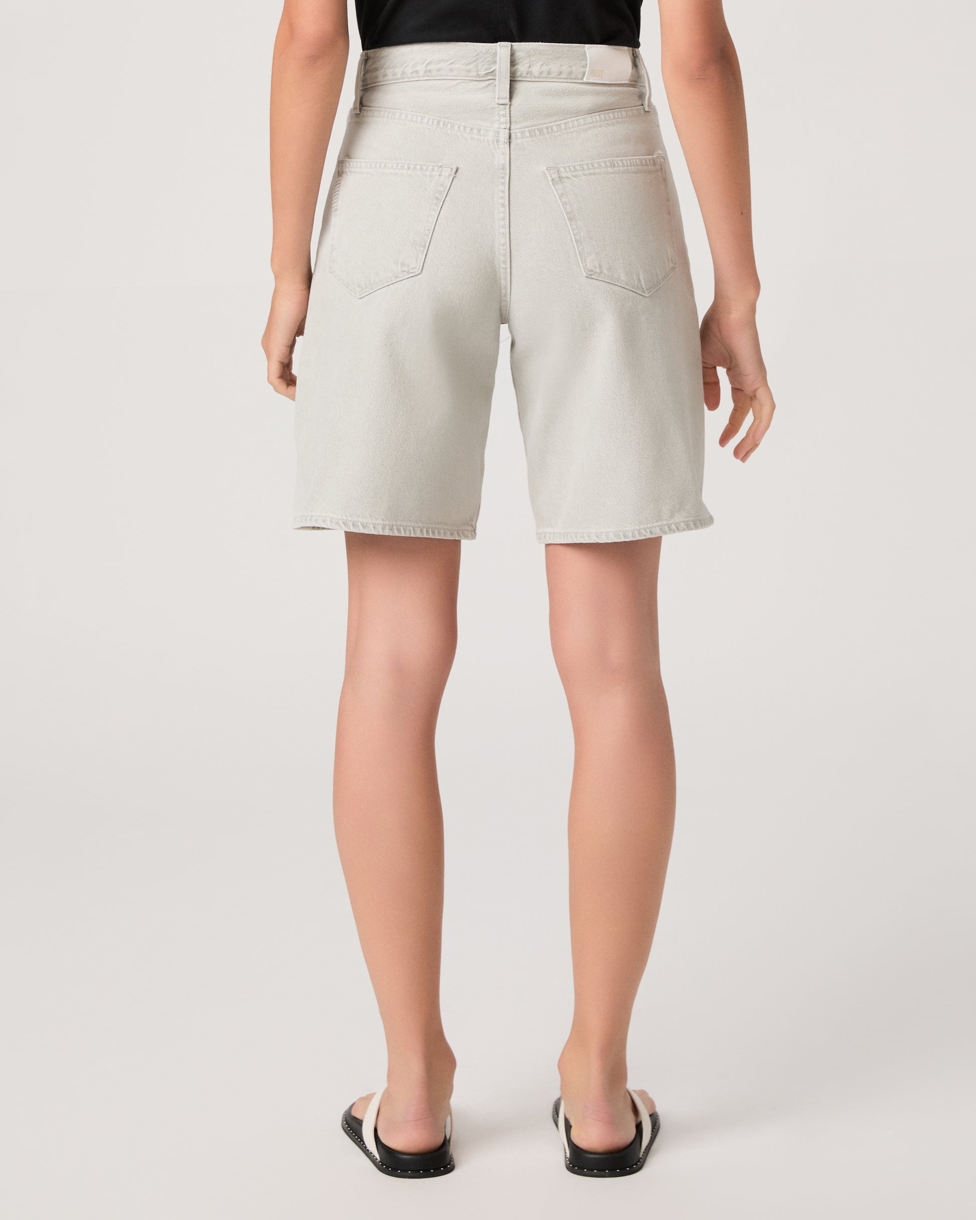 Woman wearing a black top and grey shorts on a white background