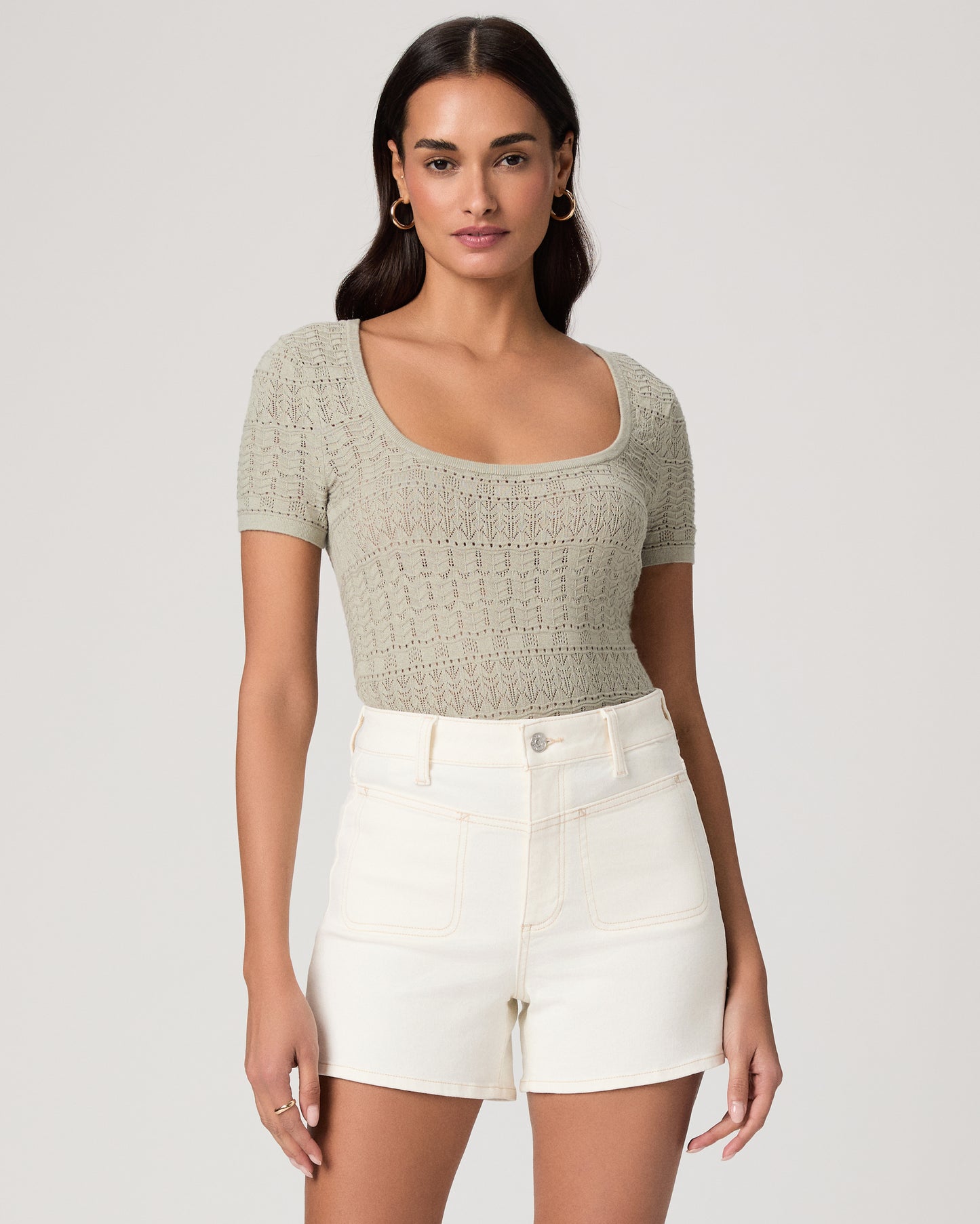 Woman wearing a green top and white shorts on a plain background