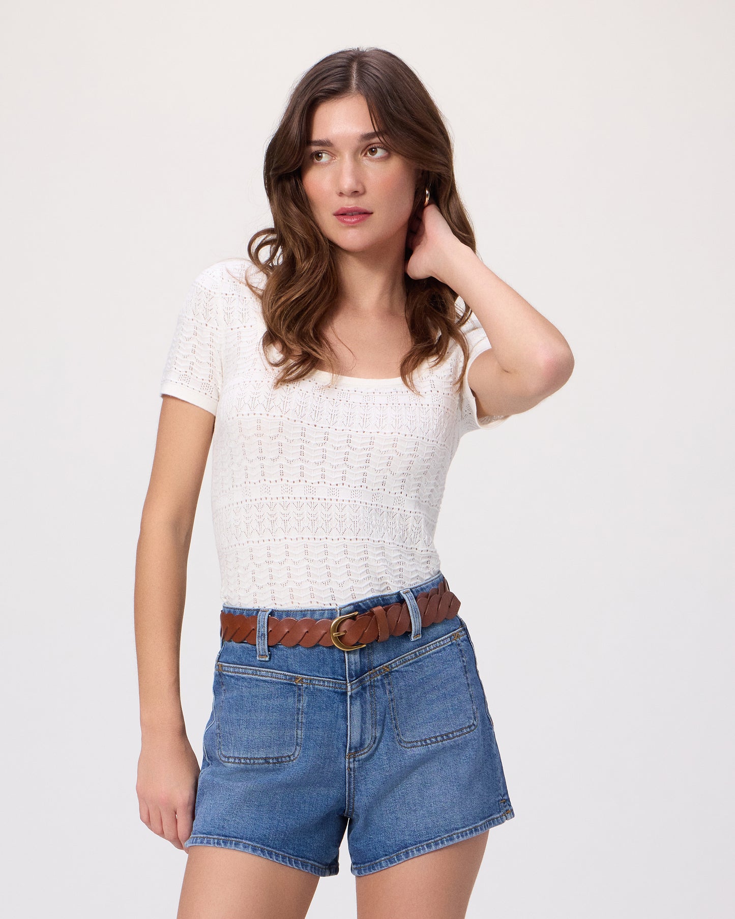 Woman wearing a white top and blue denim shorts paired with a brown belt on a white background