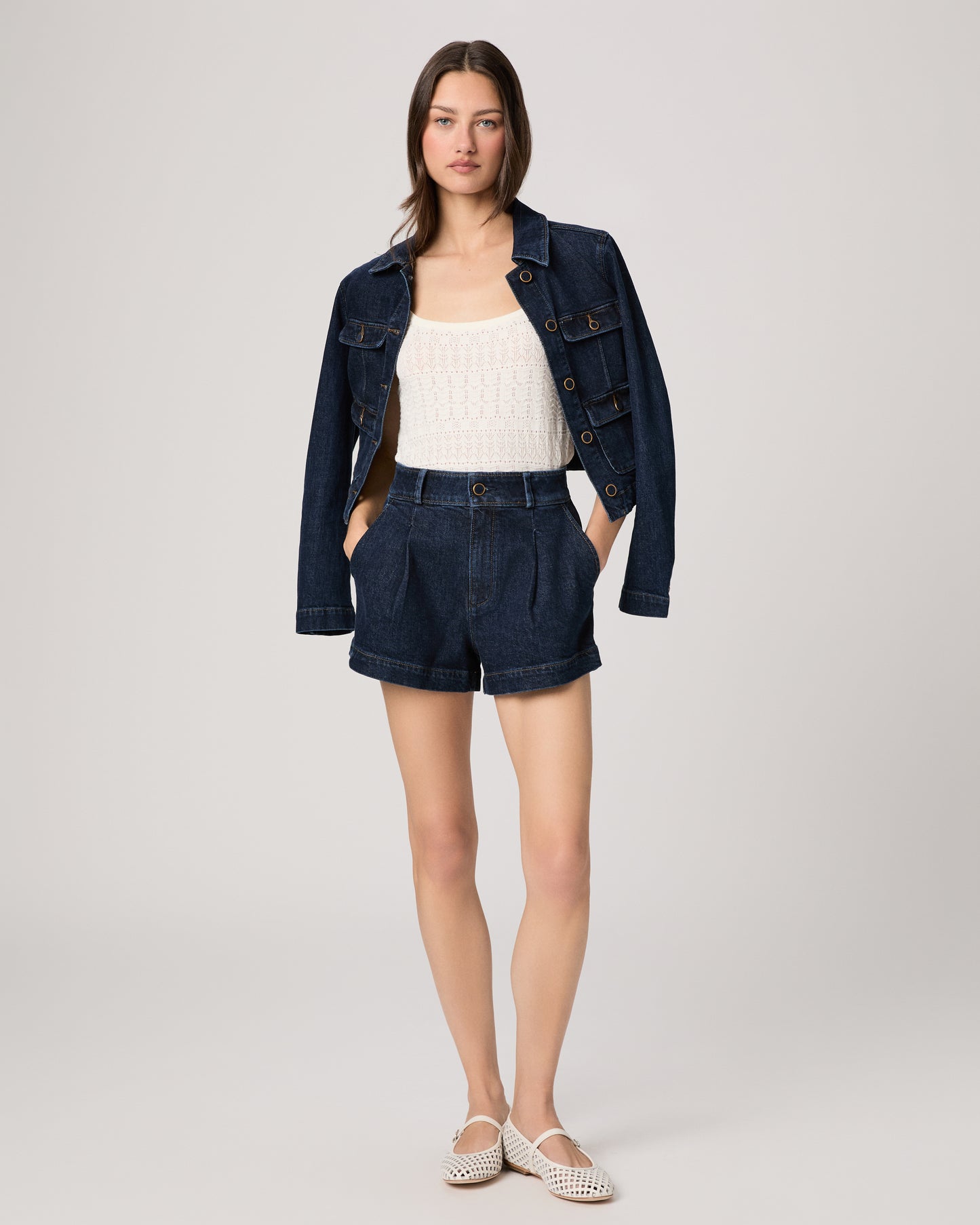 Woman wearing a white top, denim jacket and shorts on a plain background