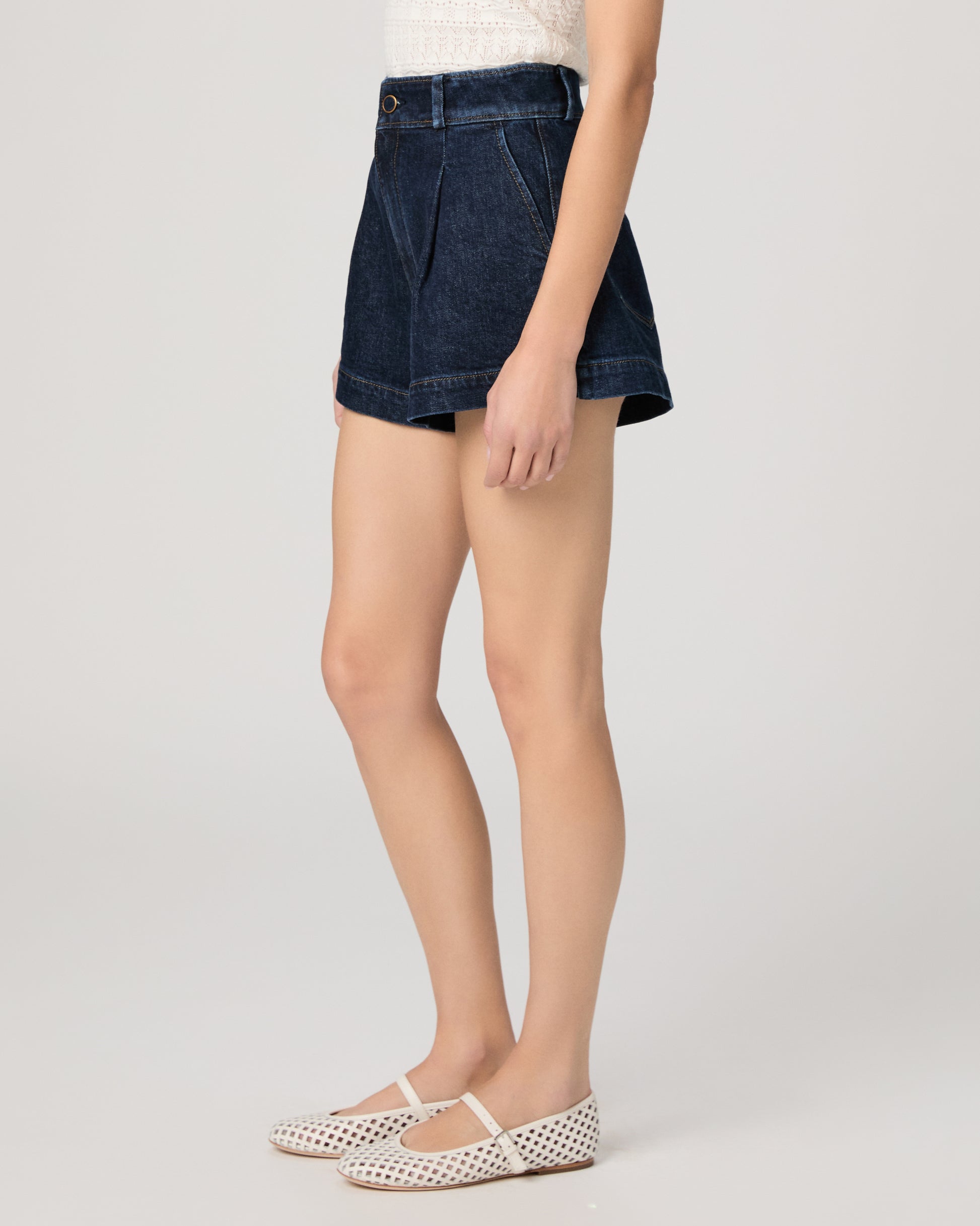 Woman wearing a white top and shorts on a plain background