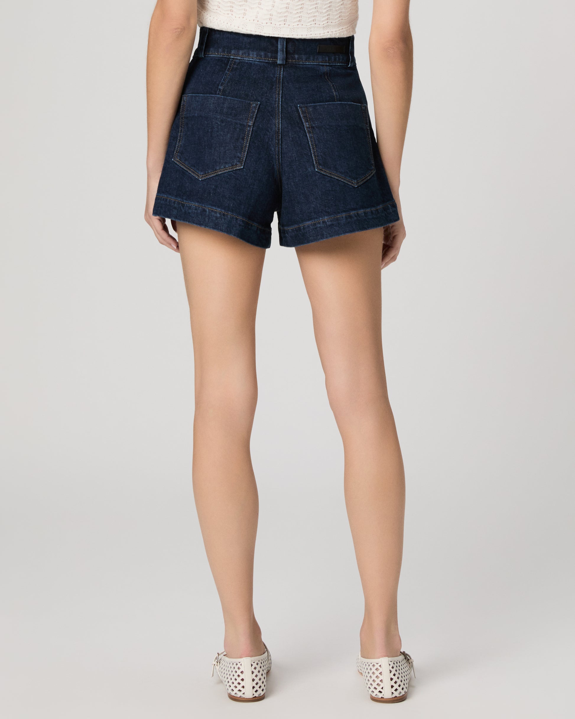 Woman wearing a white top and shorts on a plain background