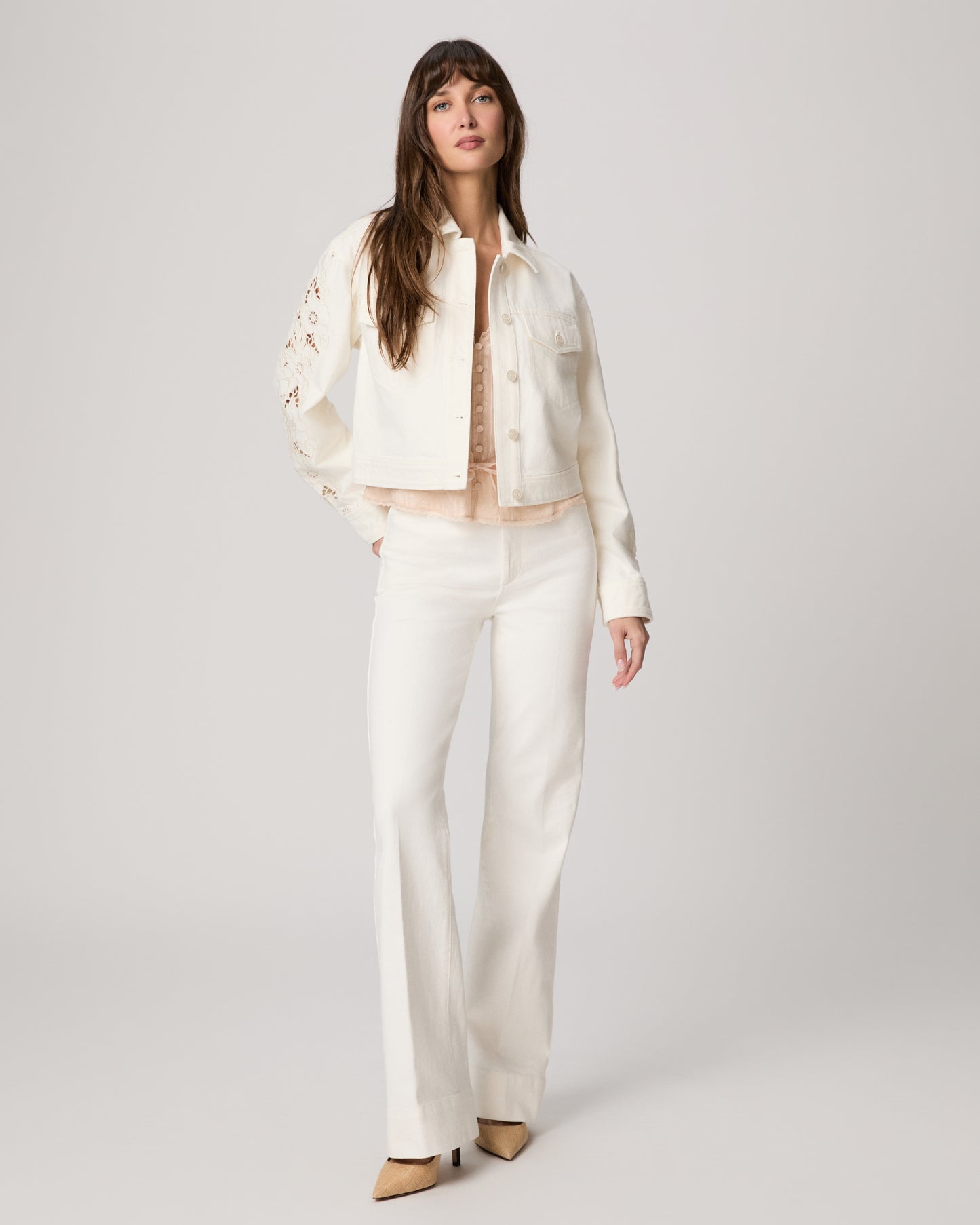 Woman wearing a white jacket and white pants paired with a pink top on a plain background