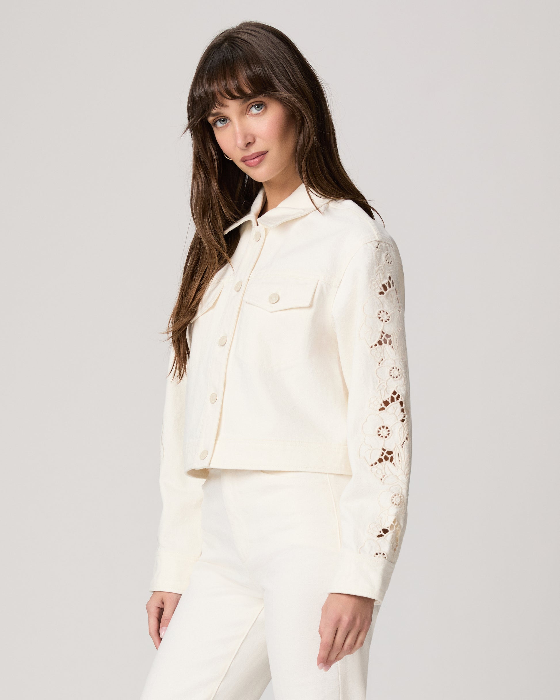 Woman wearing a white jacket and white pants paired with a pink top on a plain background