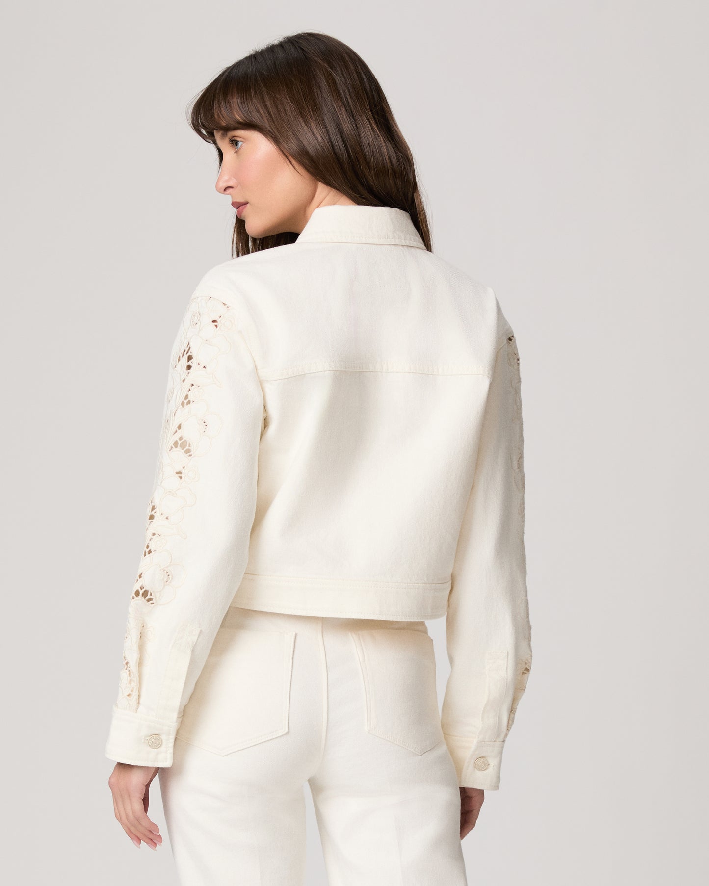 Woman wearing a white jacket and white pants paired with a pink top on a plain background