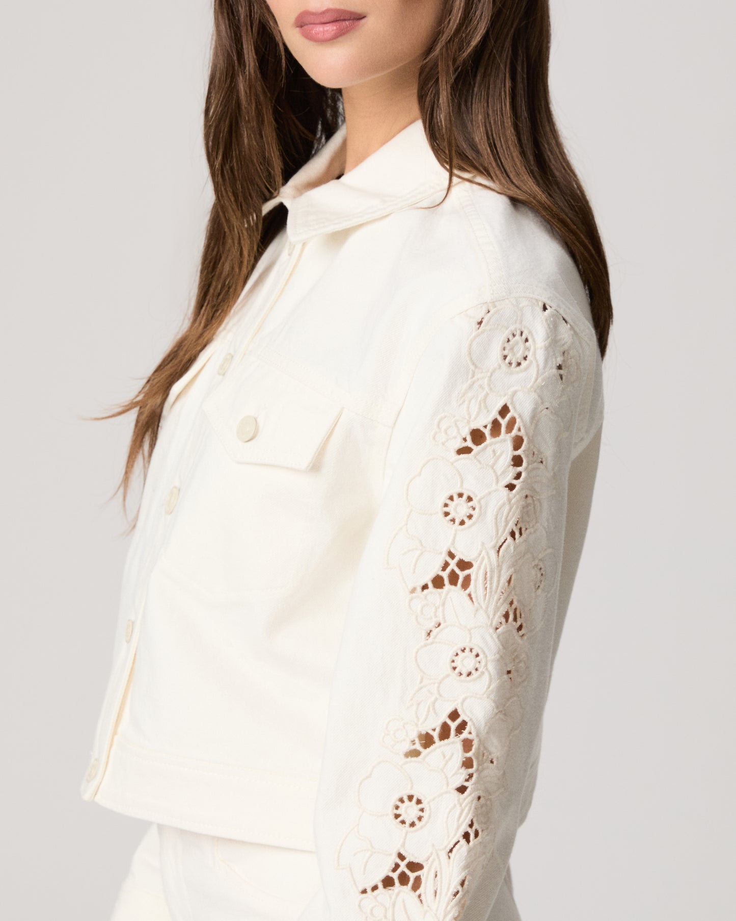 Woman wearing a white jacket and white pants paired with a pink top on a plain background