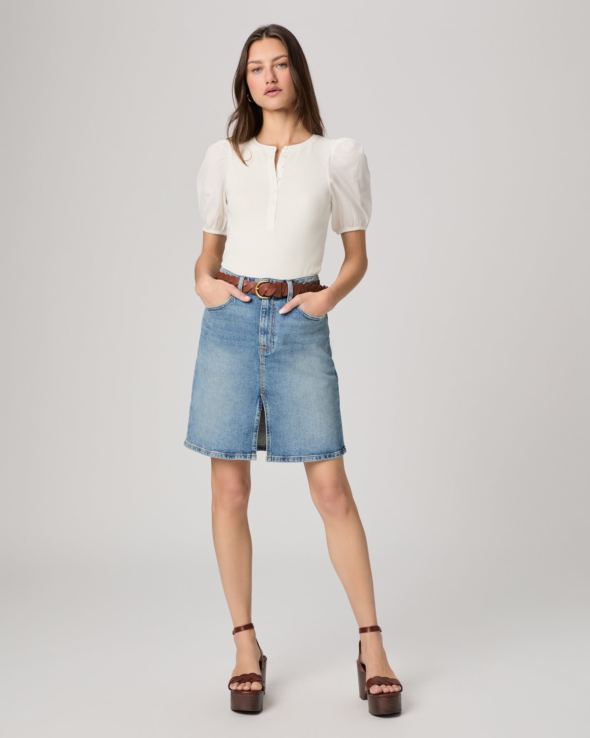 Woman wearing a white blouse and blue denim skirt on a gray background