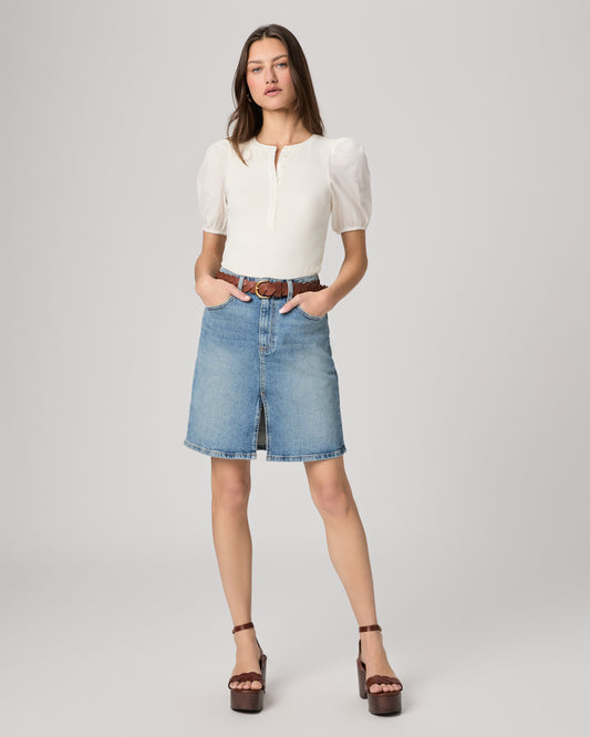 Woman wearing a white blouse and blue denim skirt on a gray background