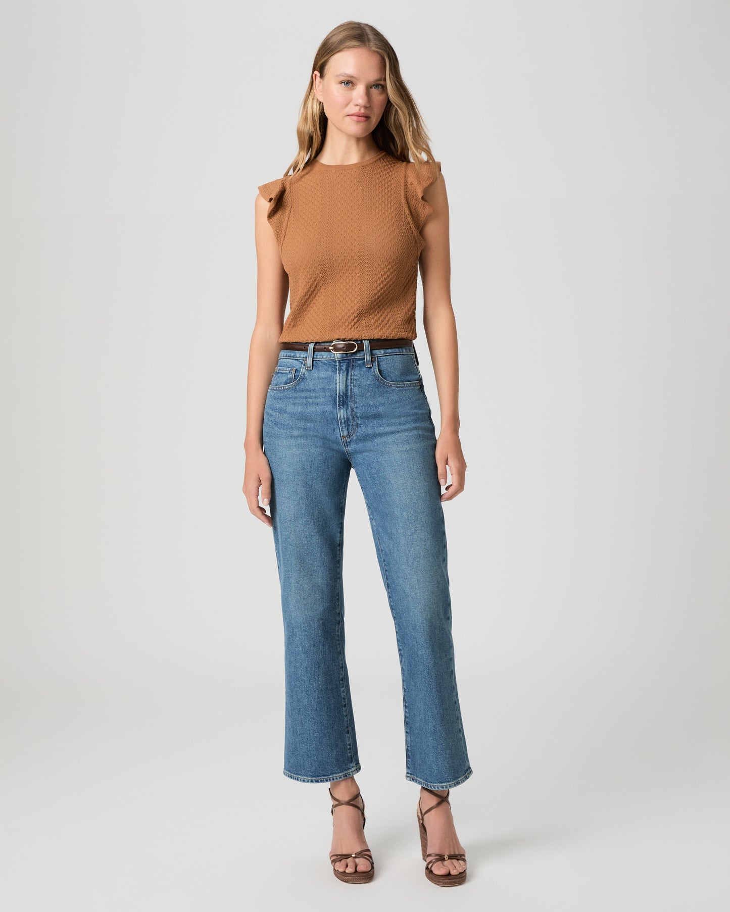 Women wearing a brown color top paired with medium wash denim and brown heels against a white background