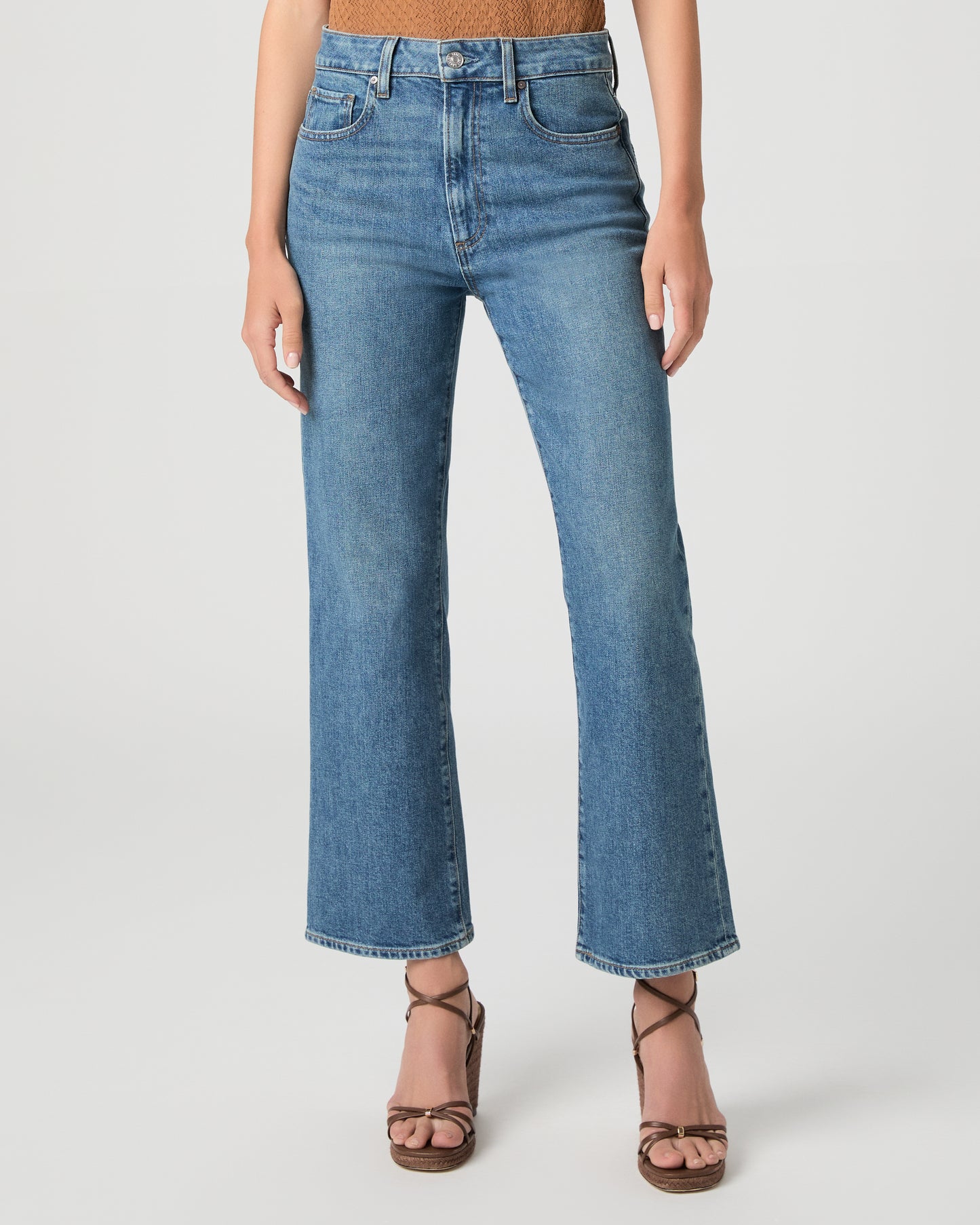 Women wearing a brown color top paired with medium wash denim and brown heels against a white background