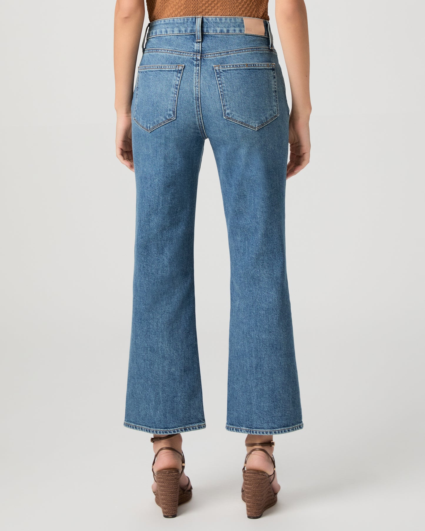 Women wearing a brown color top paired with medium wash denim and brown heels against a white background
