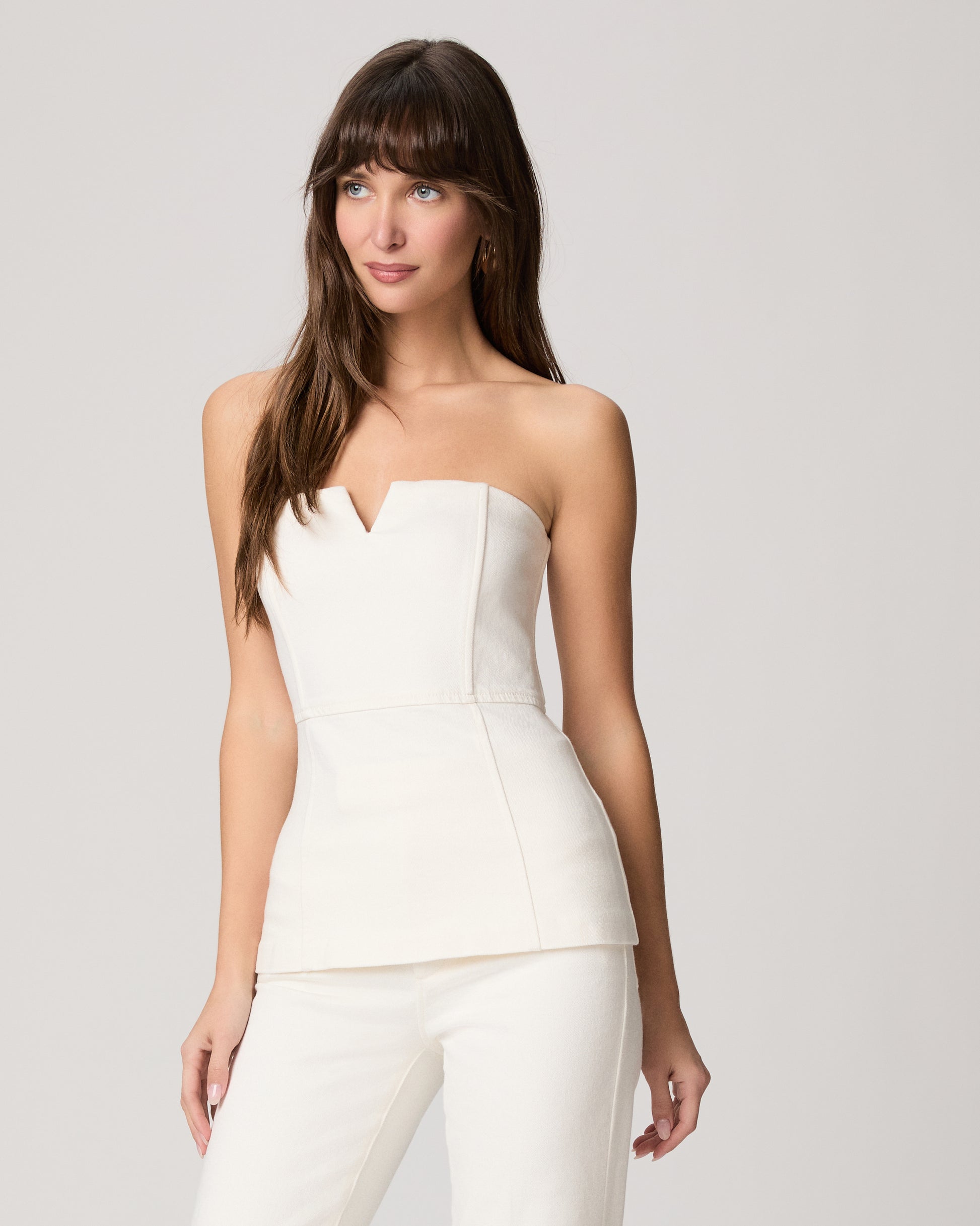 Woman wearing a white strapless top and pants on a light gray background