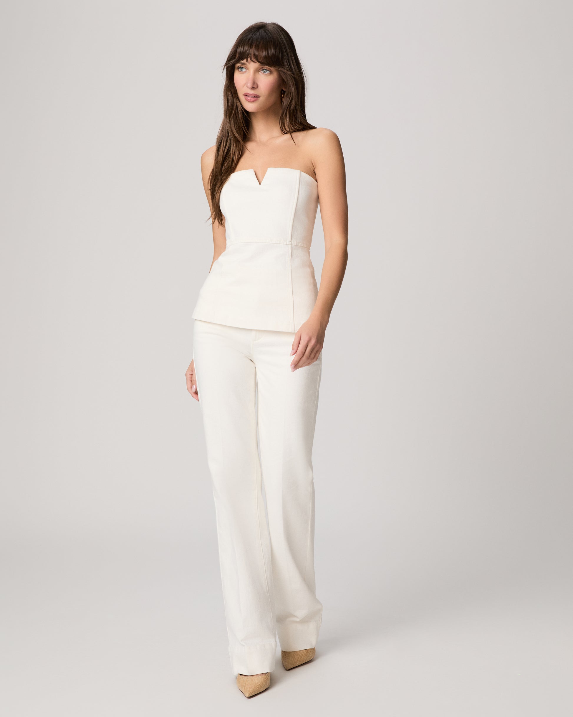 Woman wearing a white strapless top and pants on a light gray background