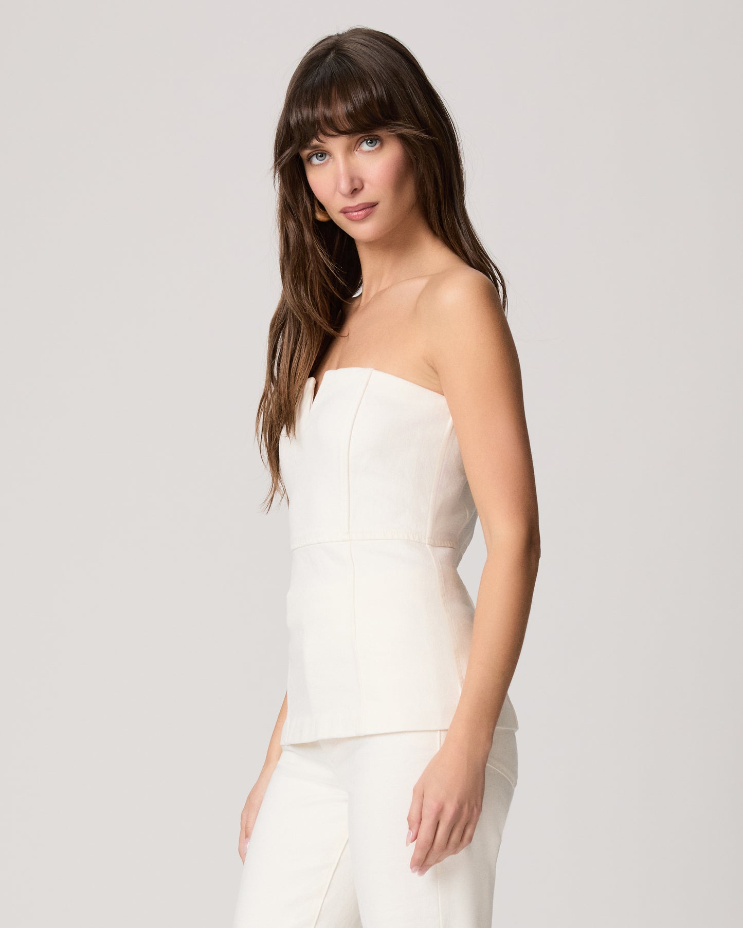 Woman wearing a white strapless top and pants on a light gray background