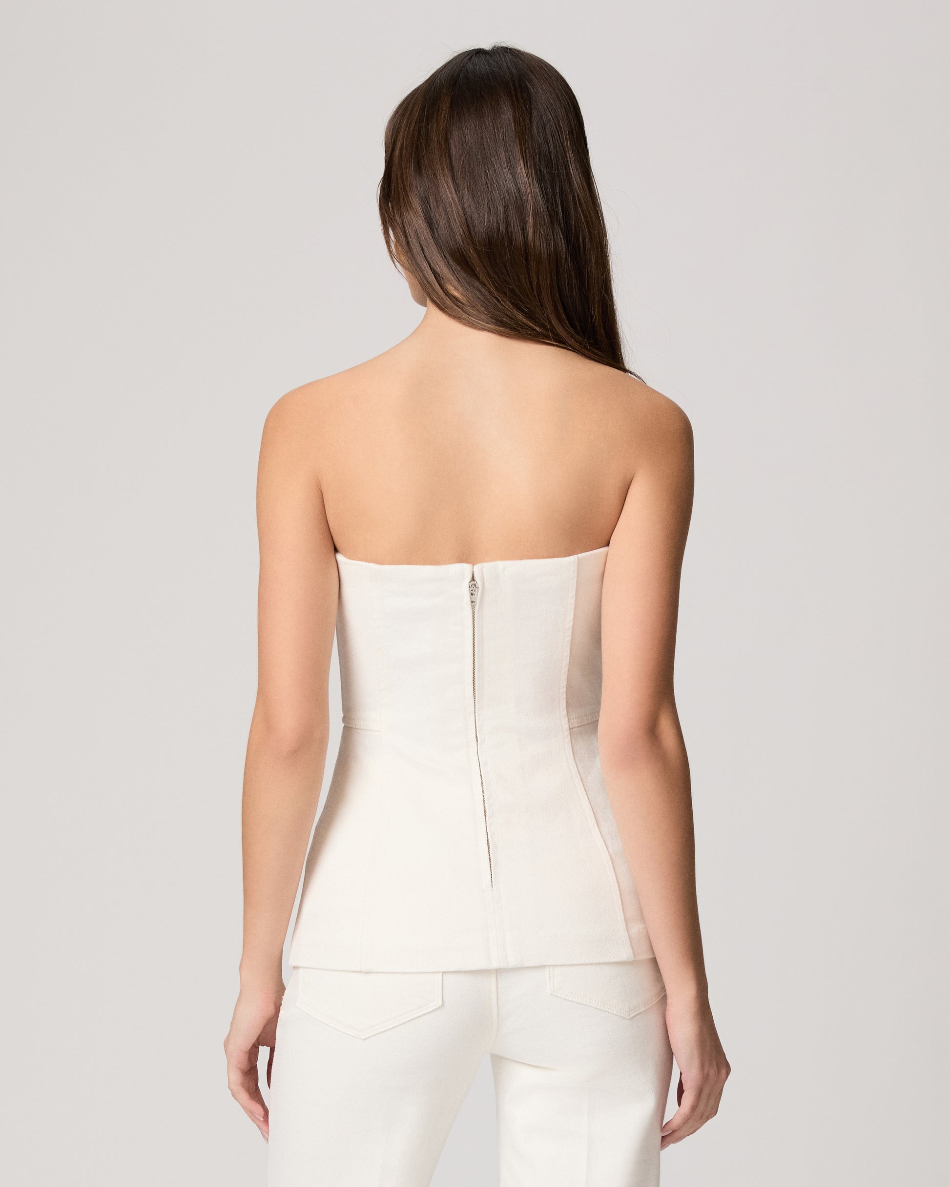 Woman wearing a white strapless top and pants on a light gray background