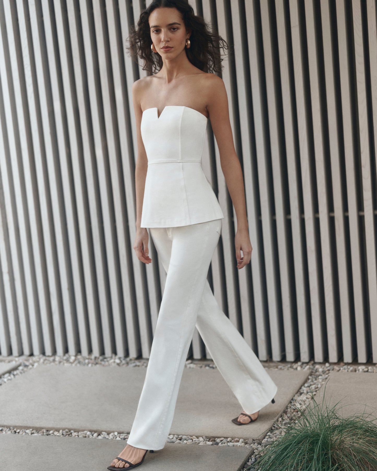 Woman wearing a white strapless top and pants against a striped wall.