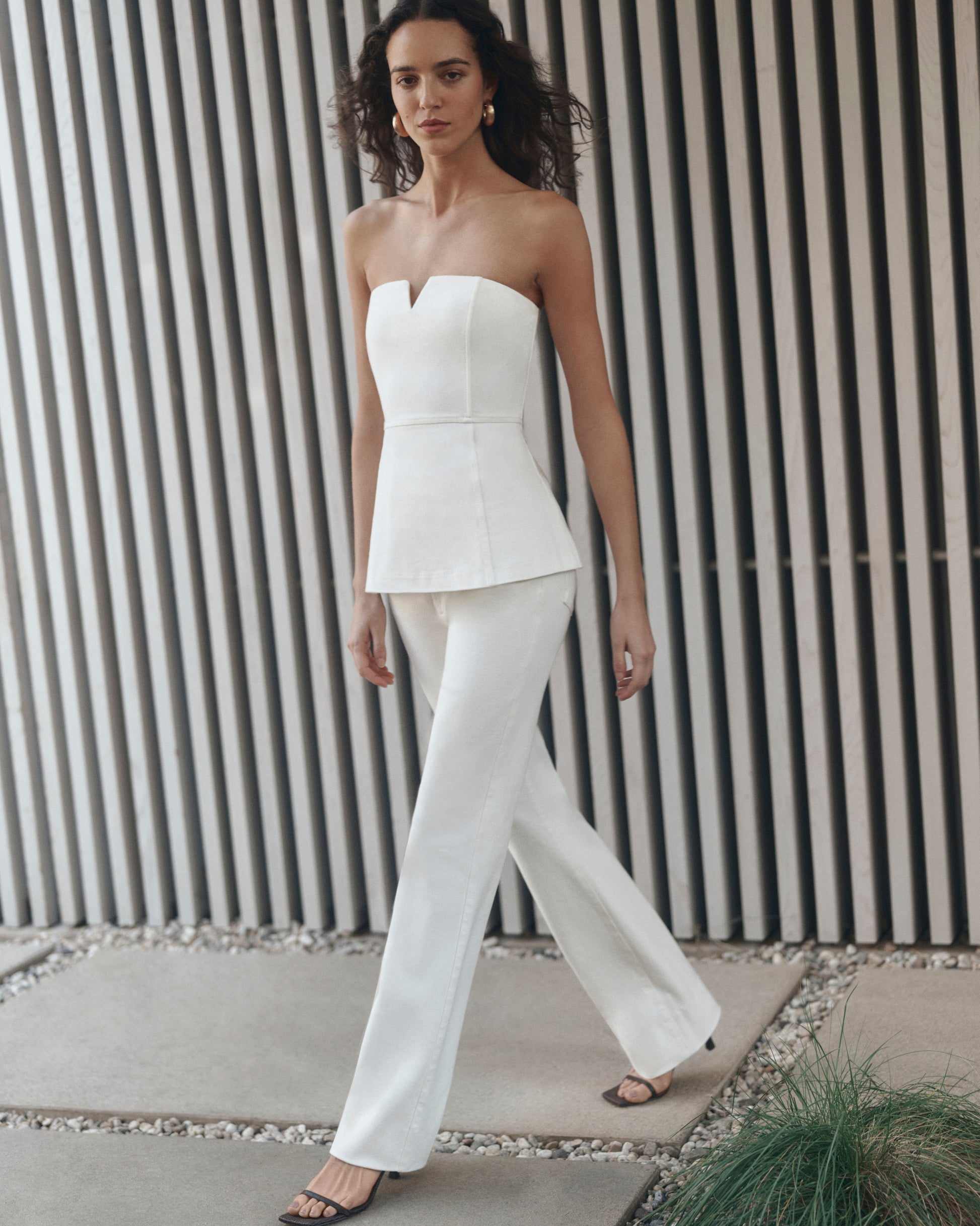 Woman wearing a white strapless top and pants against a striped wall.