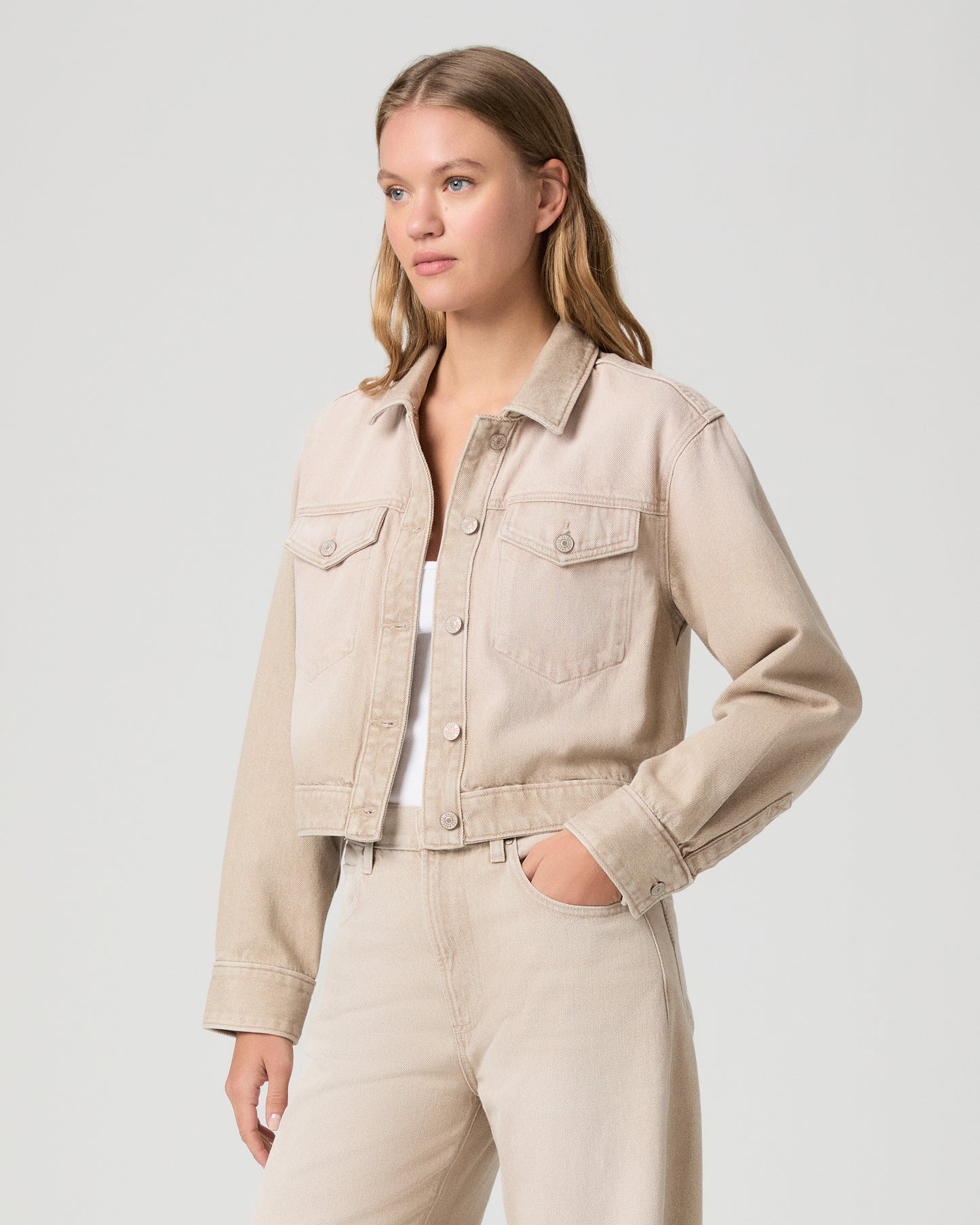 Woman wearing a beige denim jacket and pants on a light gray background