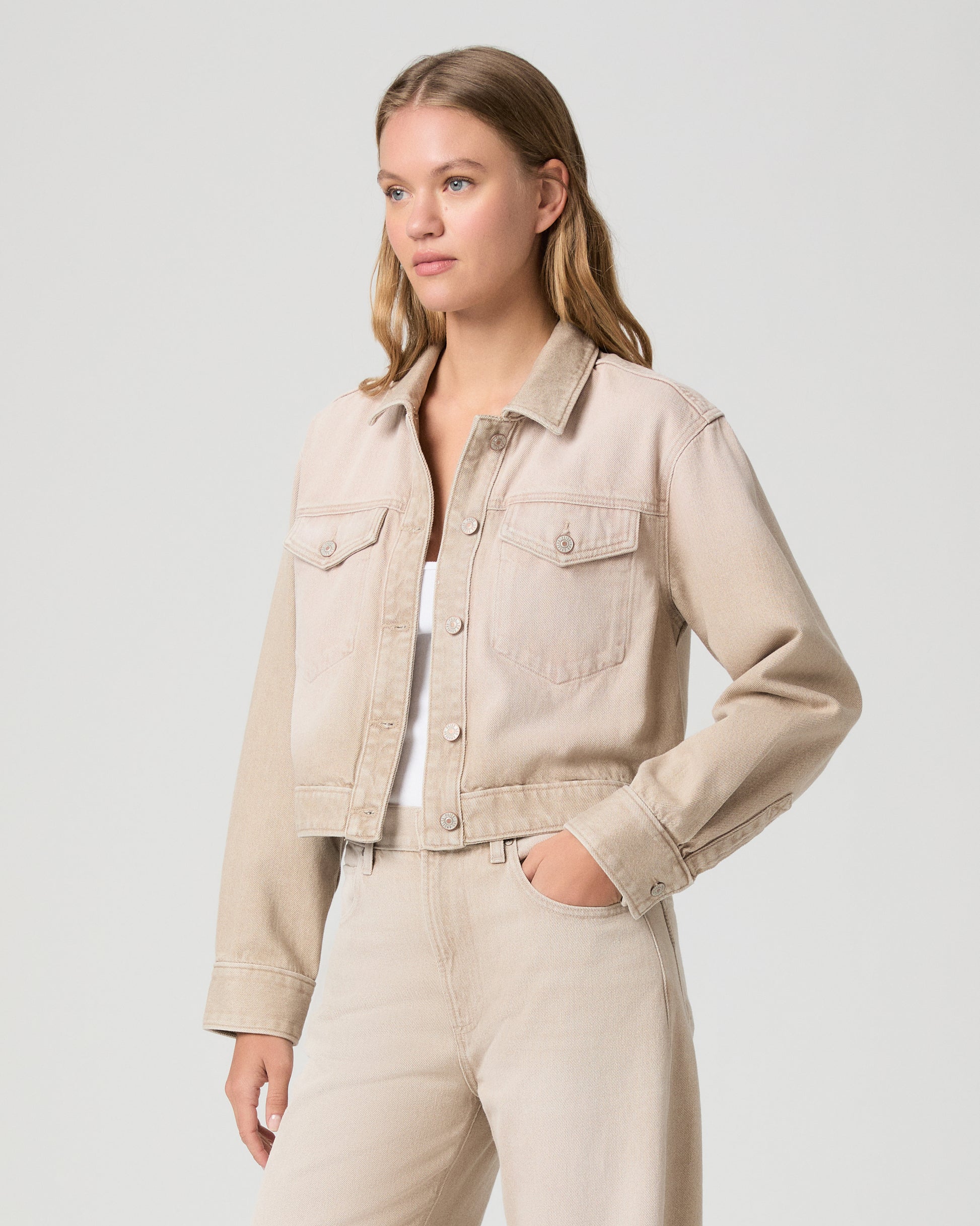 Woman wearing a beige denim jacket and pants on a light gray background