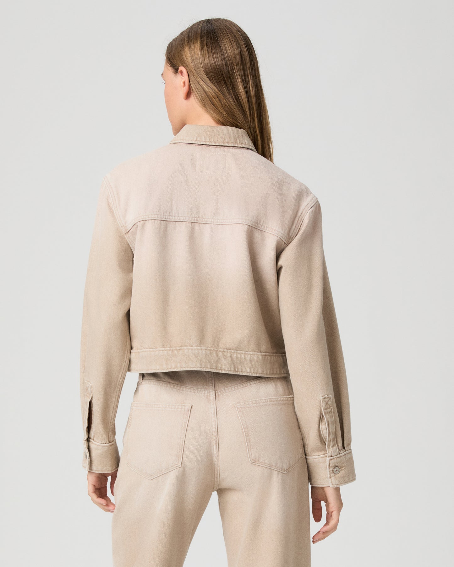 Person wearing a beige jacket and pants on a light gray background