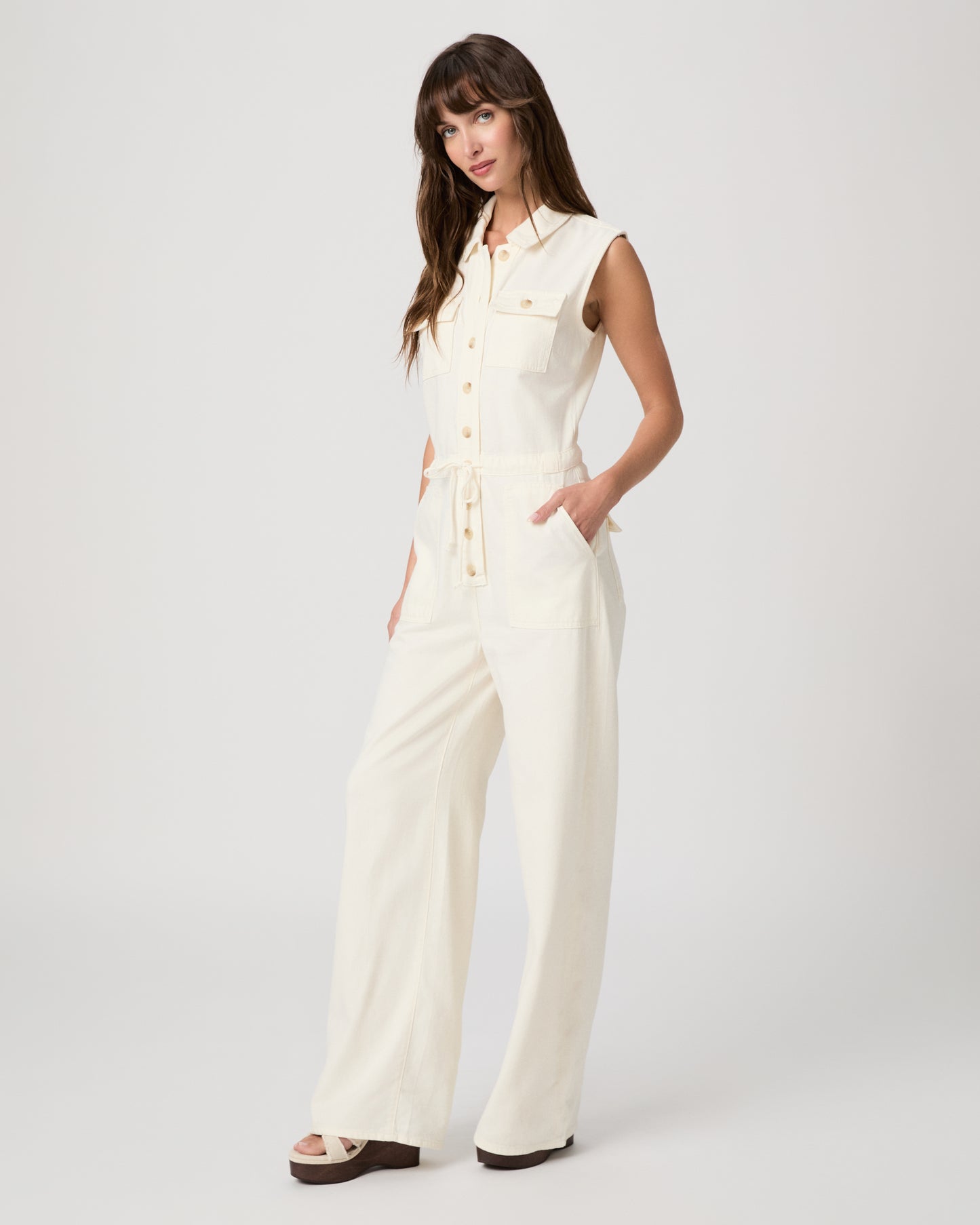 Woman wearing a white sleeveless jumpsuit on a plain background