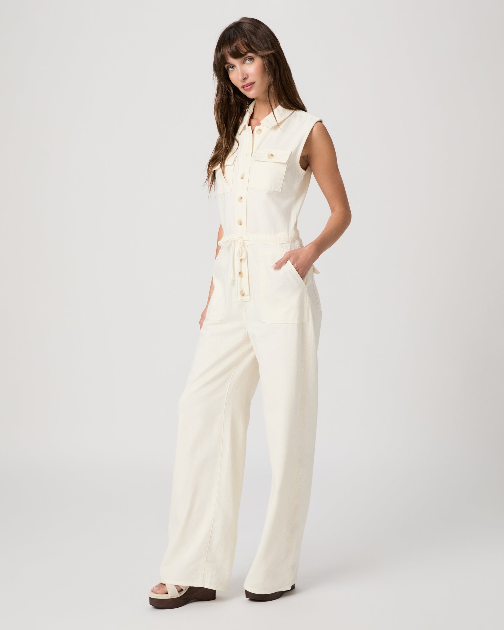 Woman wearing a white sleeveless jumpsuit on a plain background