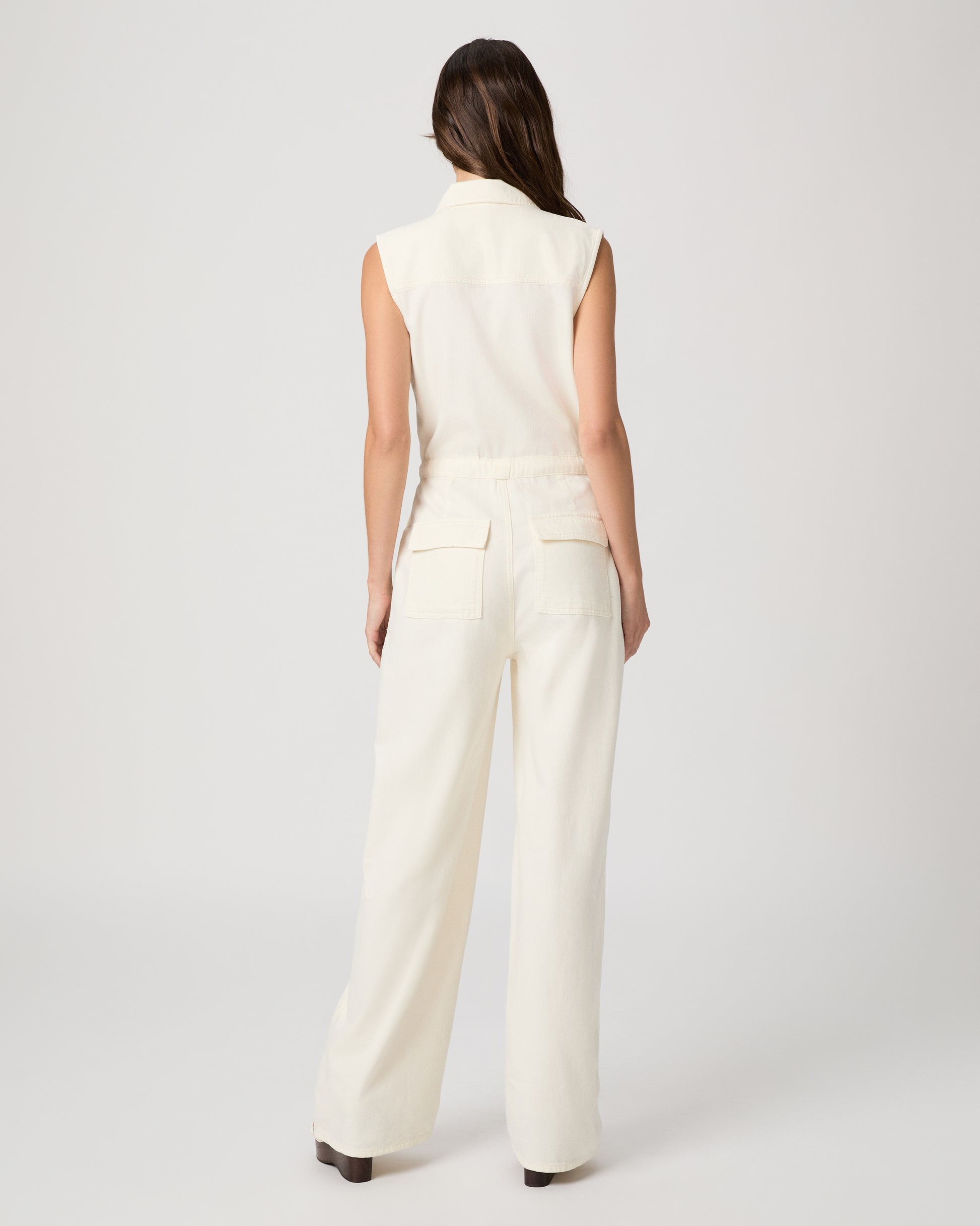 Woman wearing a white sleeveless jumpsuit on a plain background