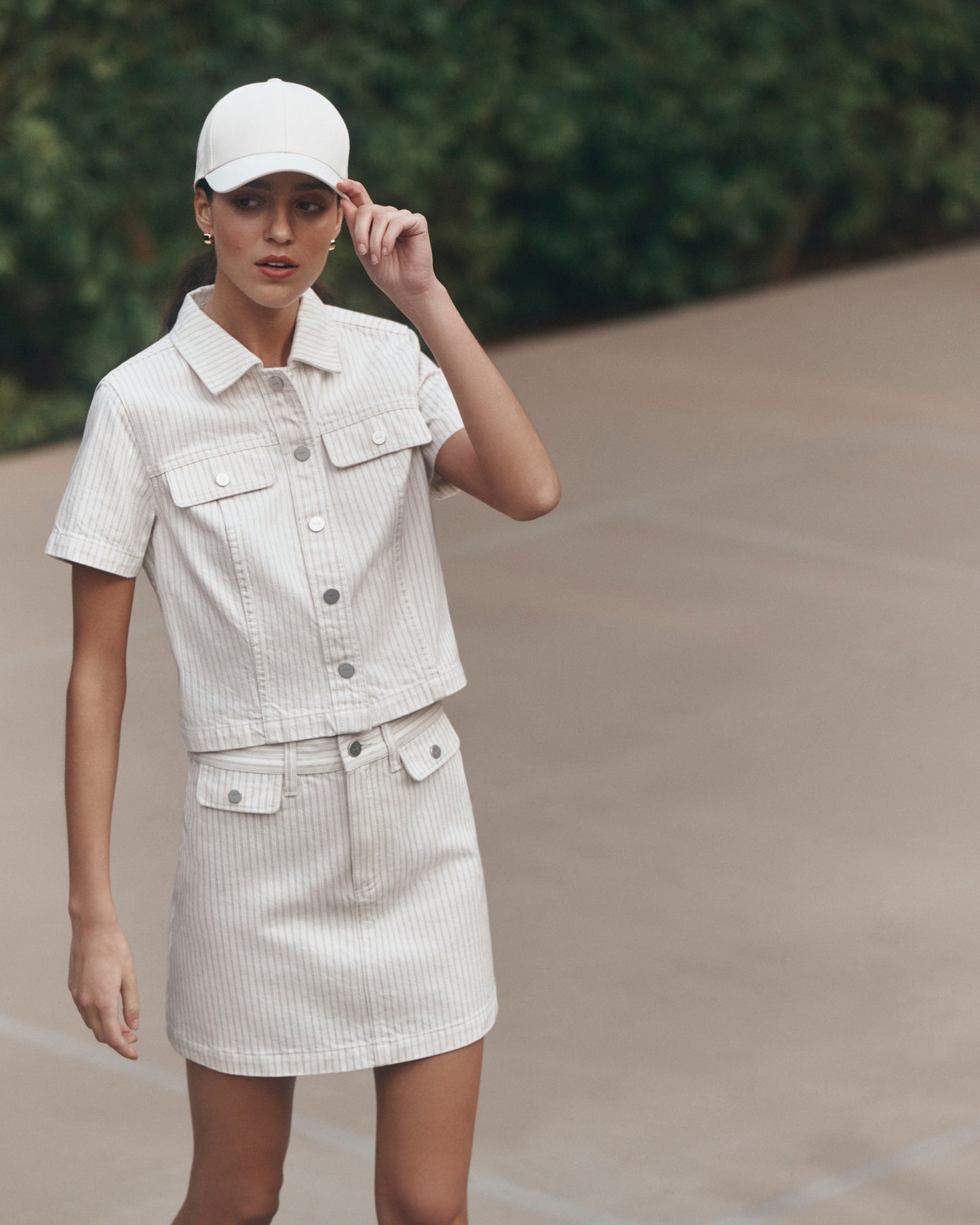 Woman wearing a matching white denim outfit with a cap outdoors.