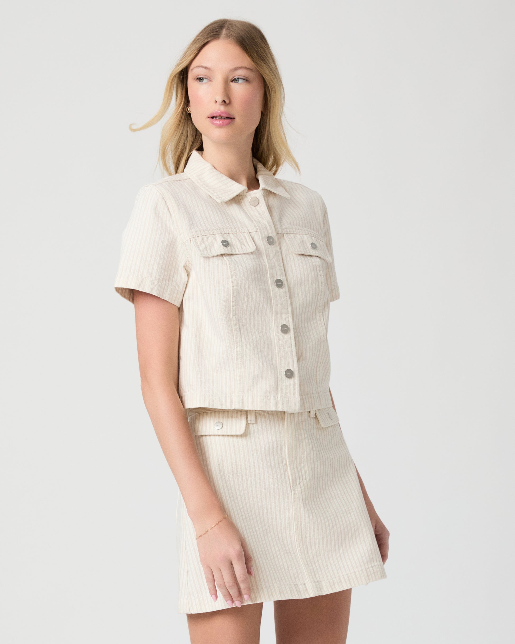Woman wearing a cream-colored jacket and skirt paired with white flats on a white background