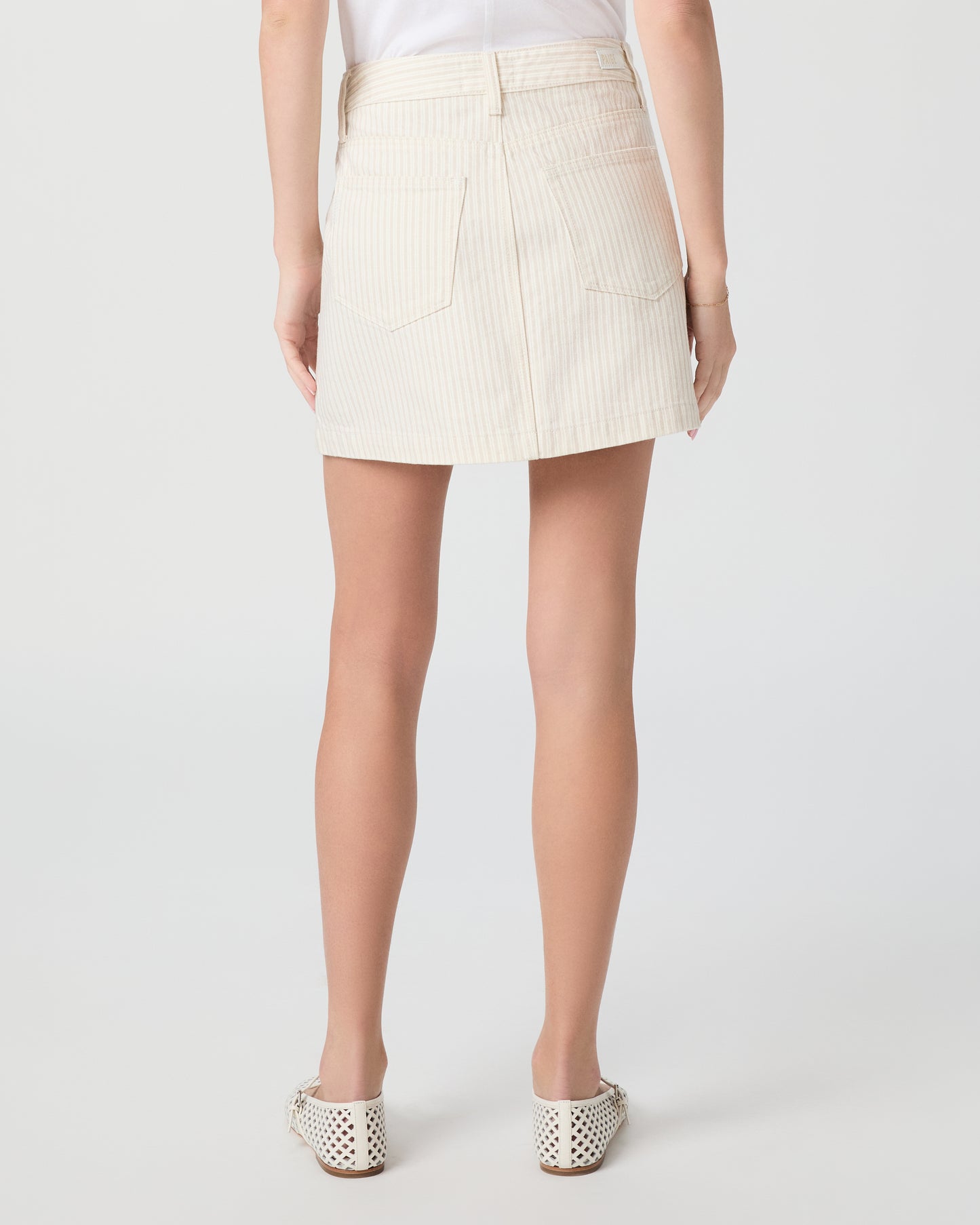 Woman wearing a cream-colored jacket and skirt paired with white flats on a white background